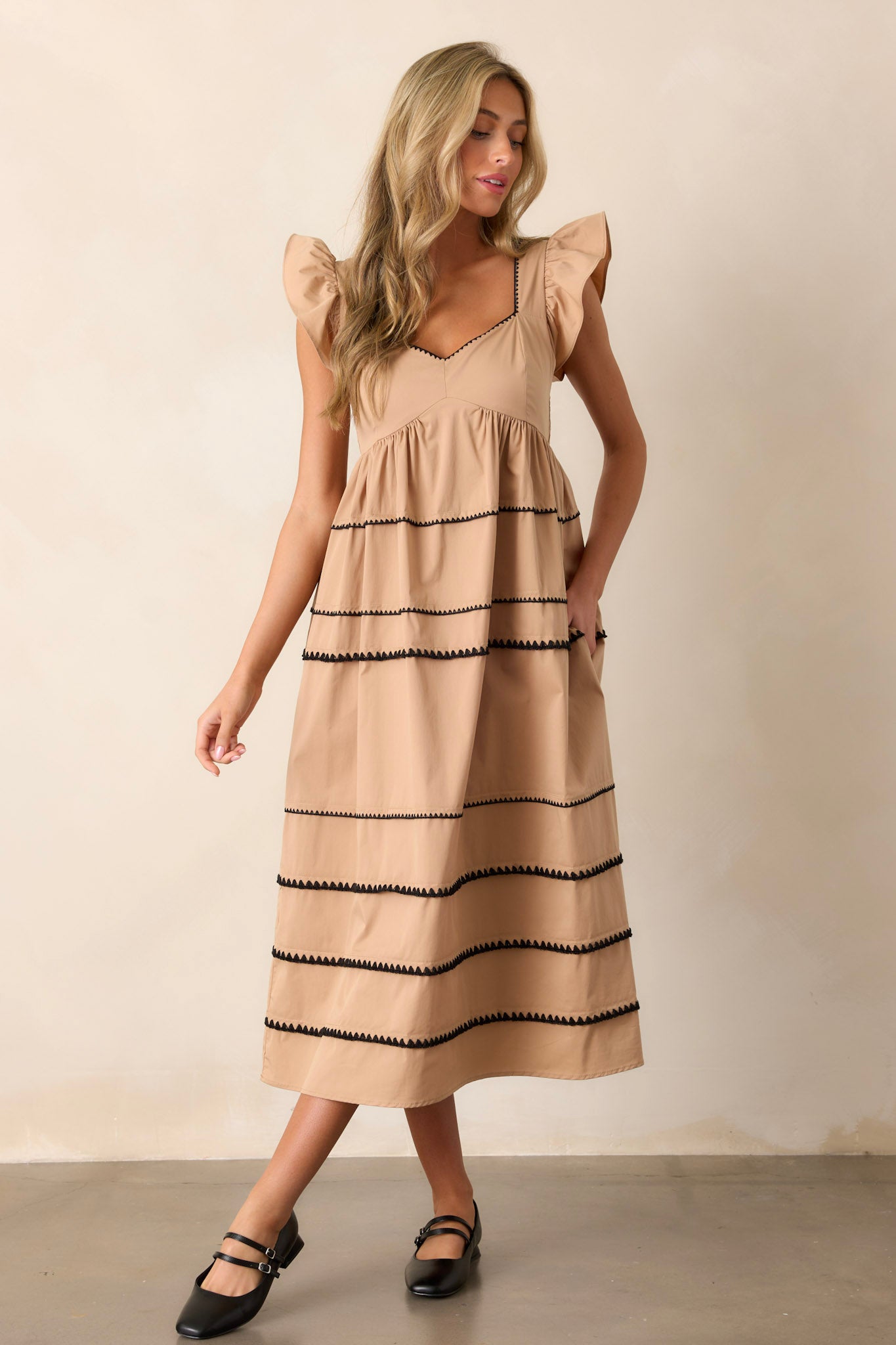 This tan dress features ruffle cap sleeves, a smocked back, multiple tiers, two functional pockets, and ric-rac detailing.