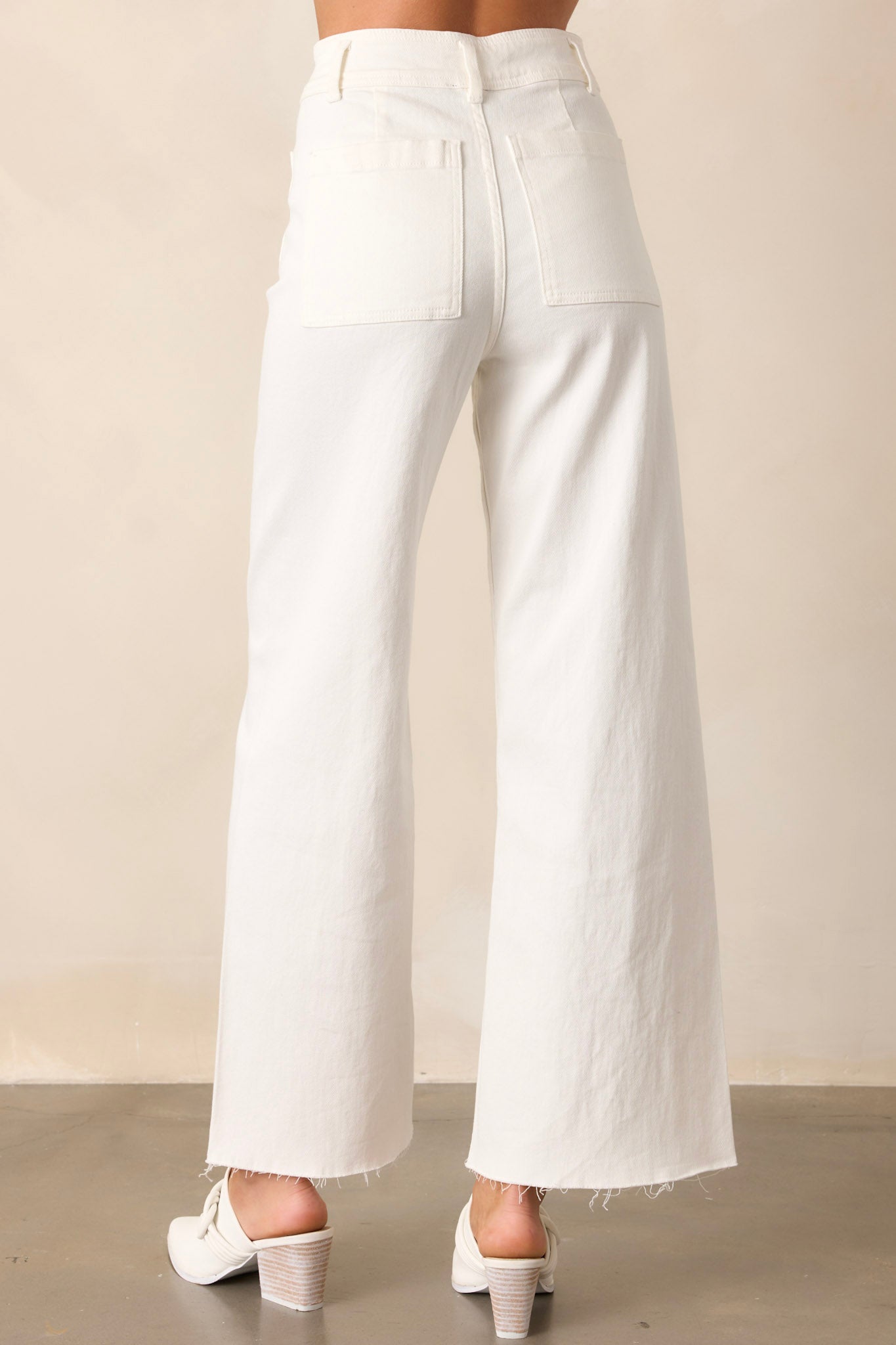 Back view of these ivory jeans that feature a high waisted design, a button & zipper closure, belt loops, functional front & back pockets, a wide leg design, and a raw hemline