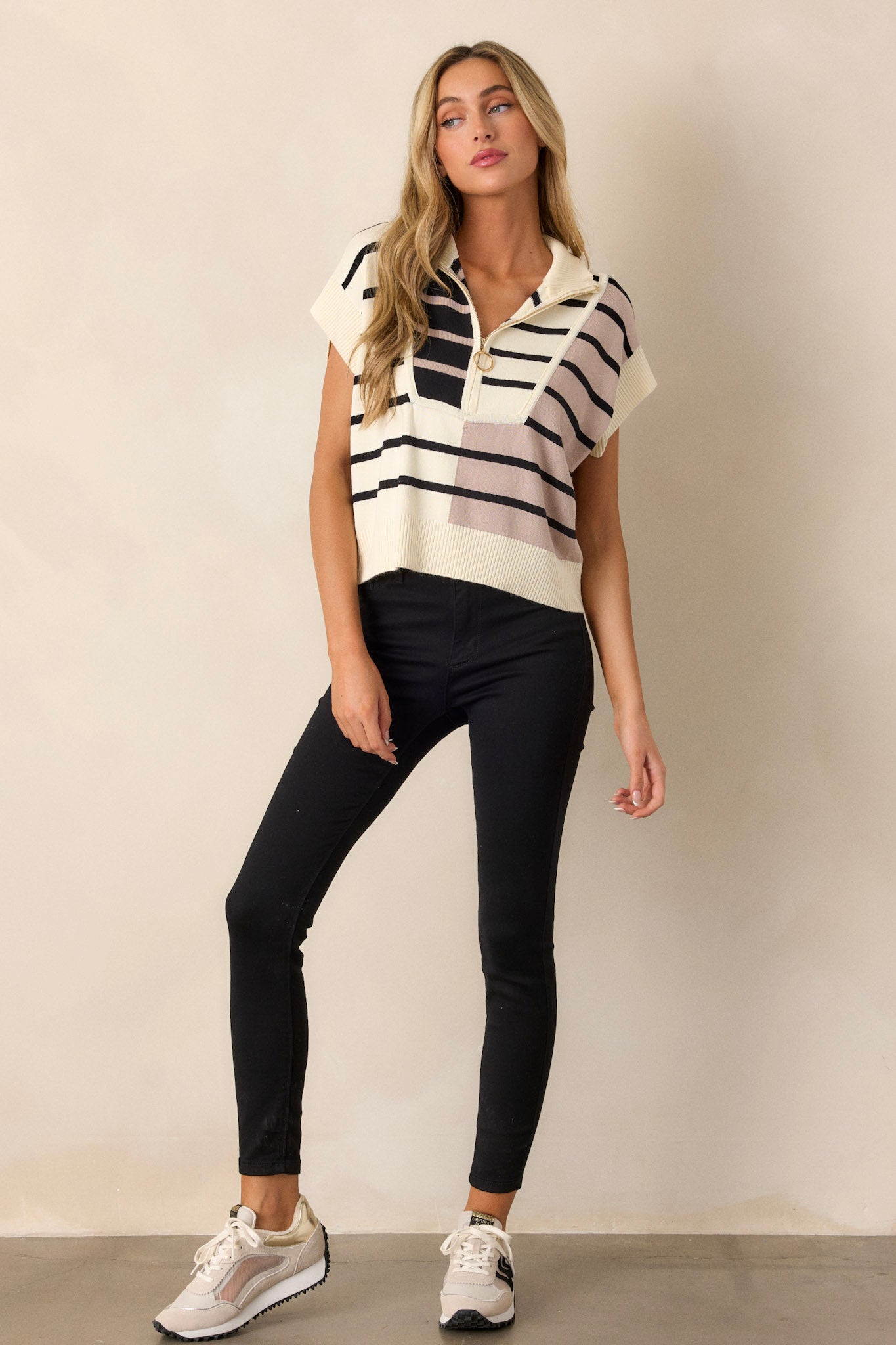 Full length view of a beige sweater with a ribbed collared neckline, gold hardware, a functional half zip design, a bold striped design, ribbed cap sleeves, and a ribbed hemline