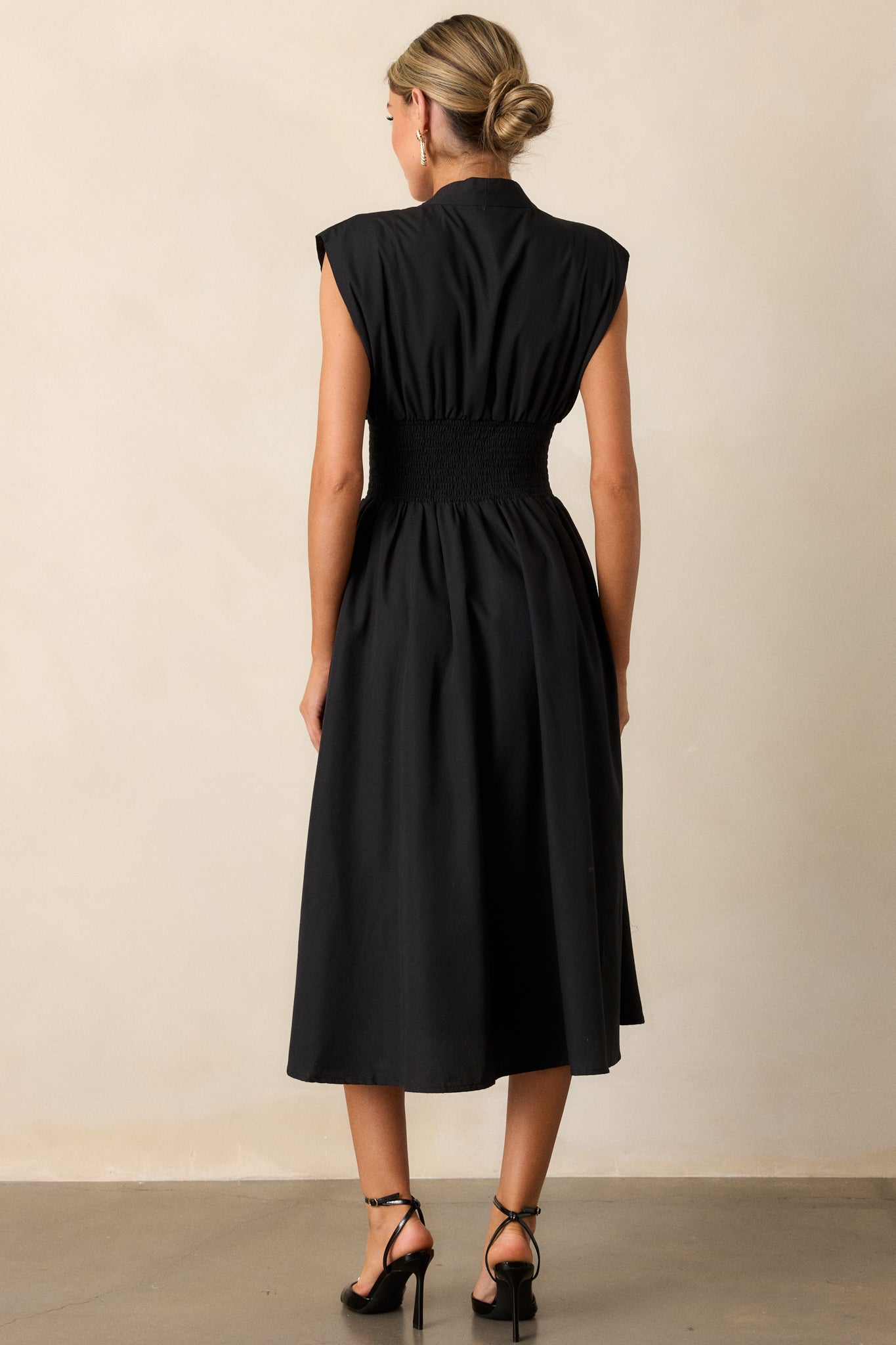 Back view of a black midi dress highlighting the overall fit, padded shoulders, and fully smocked waist.