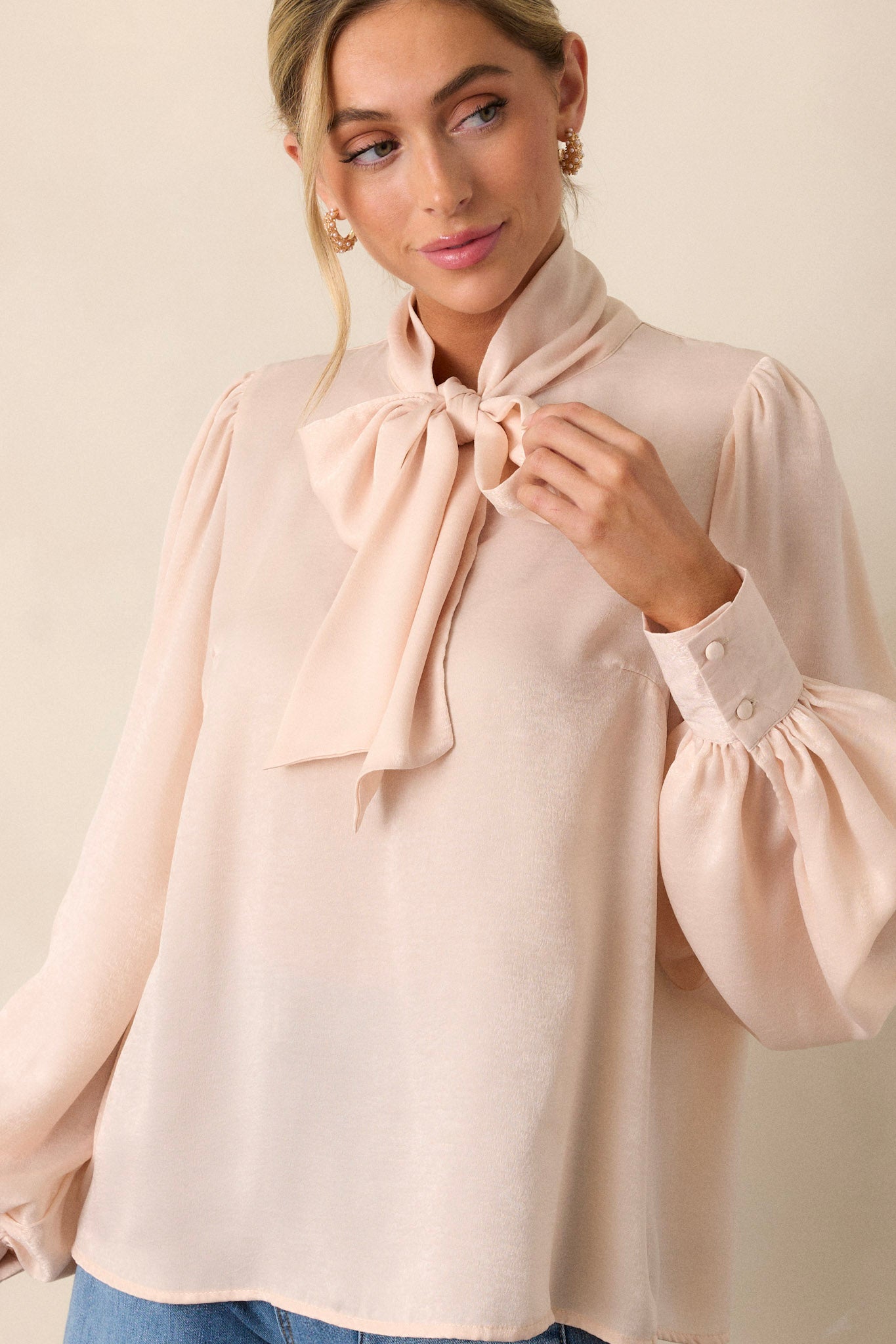 Front angled view of a top featuring a high neckline with an adjustable self-tie, flowy balloon sleeves with two buttons at the cuff, and a relaxed fit.