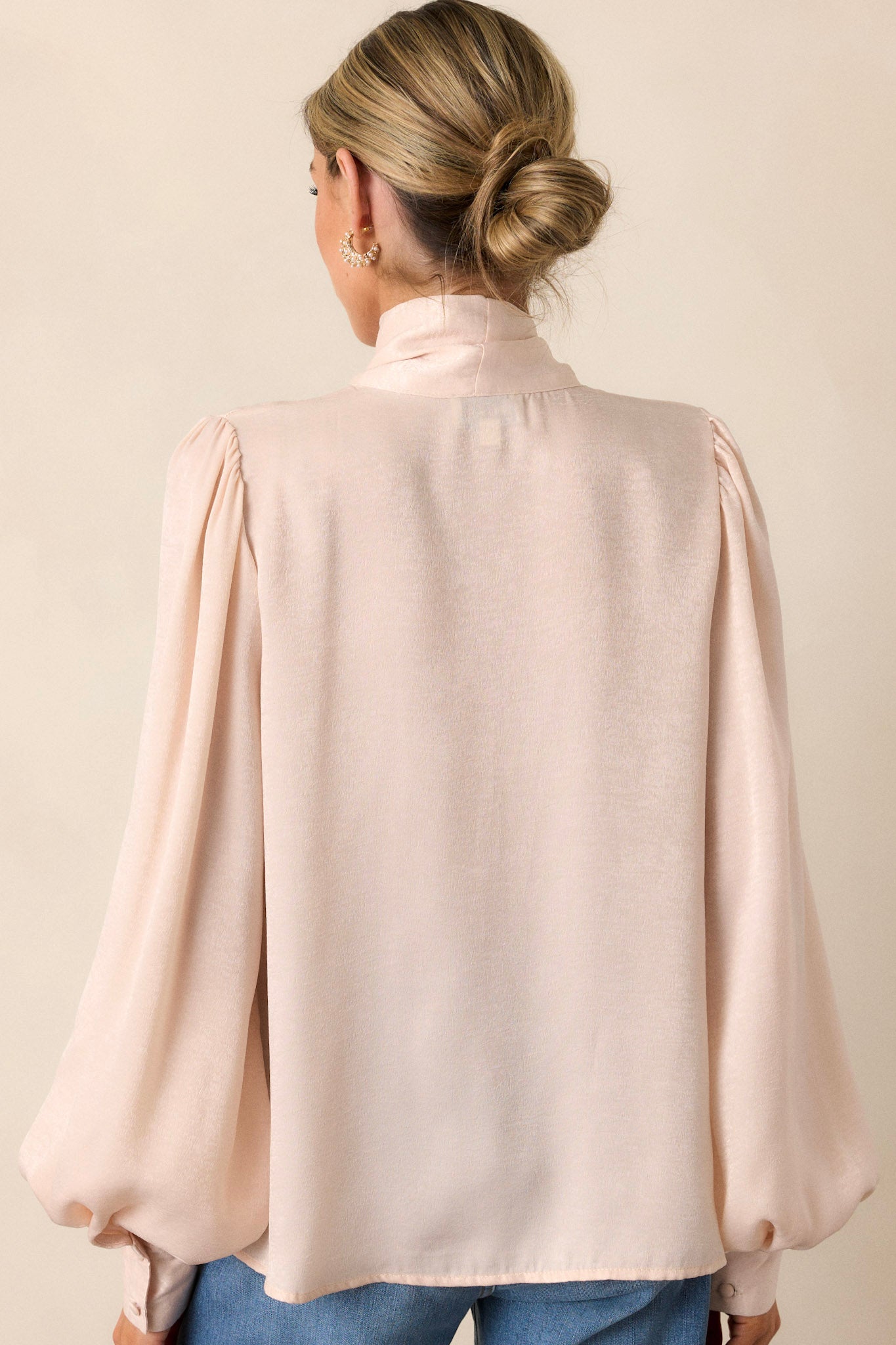 Back view of a top highlighting the adjustable self-tie at the high neckline and the flowy balloon sleeves with buttoned cuffs.