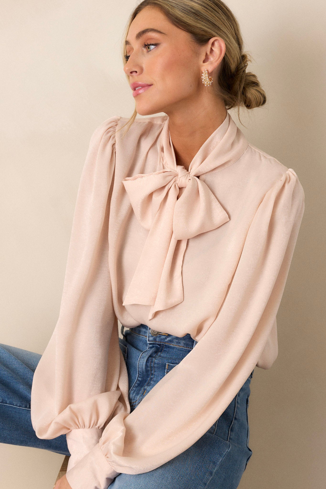 This top features a high neckline with an adjustable self tie, flowy balloon sleeves with two buttons at the cuff, and a relaxed fit.