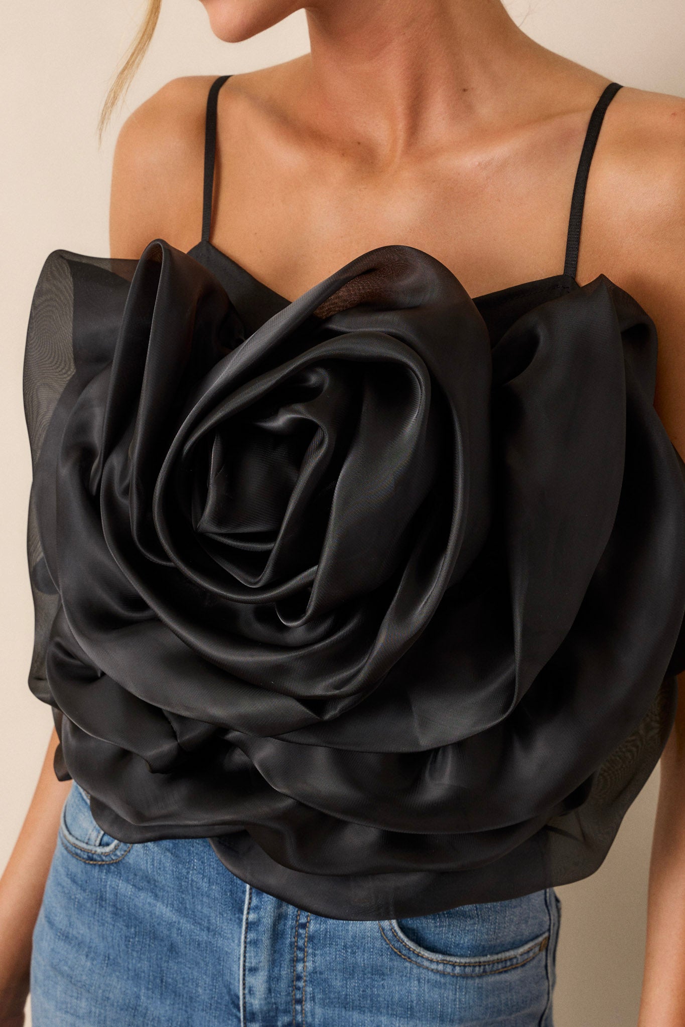 Close up view of this black crop top that features a square neckline, thin & stretchy adjustable straps, a fully smocked back, a large 3-D flower, and a cropped hemline.