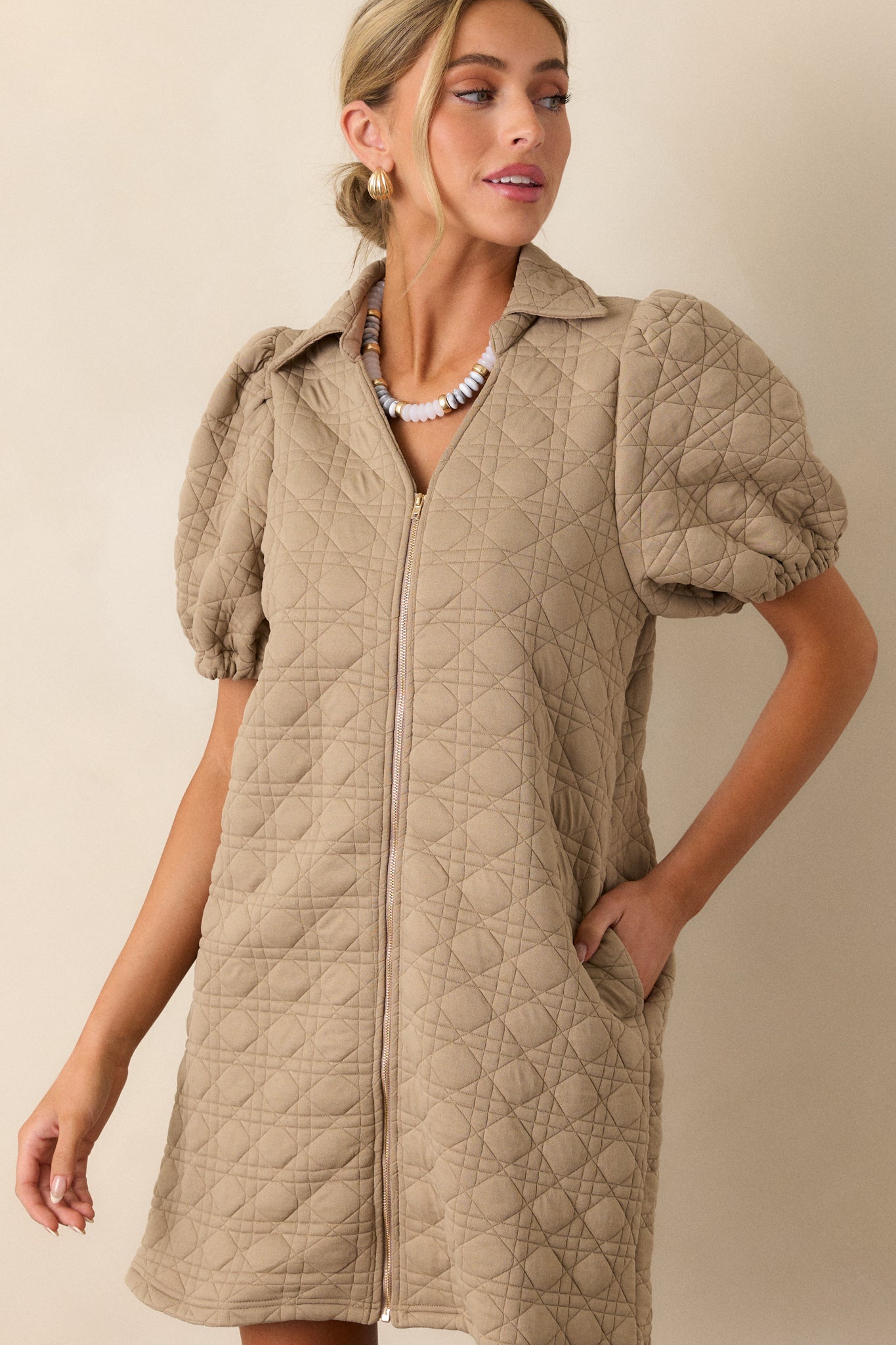 Close-up of the collared neckline and full-zip front of the tan dress, emphasizing the quilted fabric and functional zipper detail.