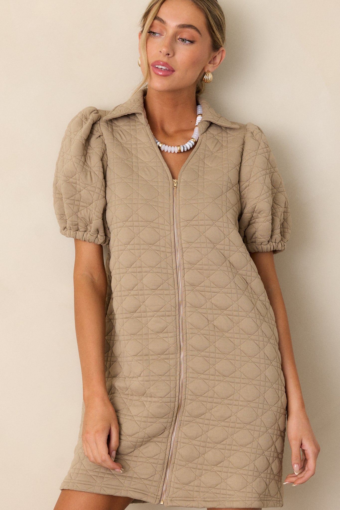 A detailed shot of the front of the tan dress, highlighting the quilted material and the clean lines of the zipper and puff sleeve design.