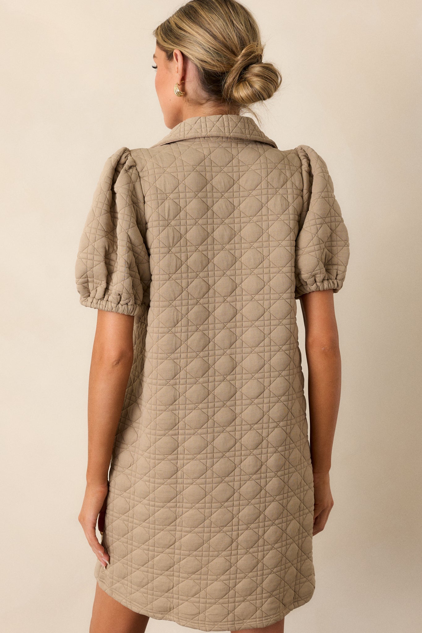 The back view of the tan mini dress, showcasing the smooth quilted fabric and the structure of the short puff sleeves and collared neckline.