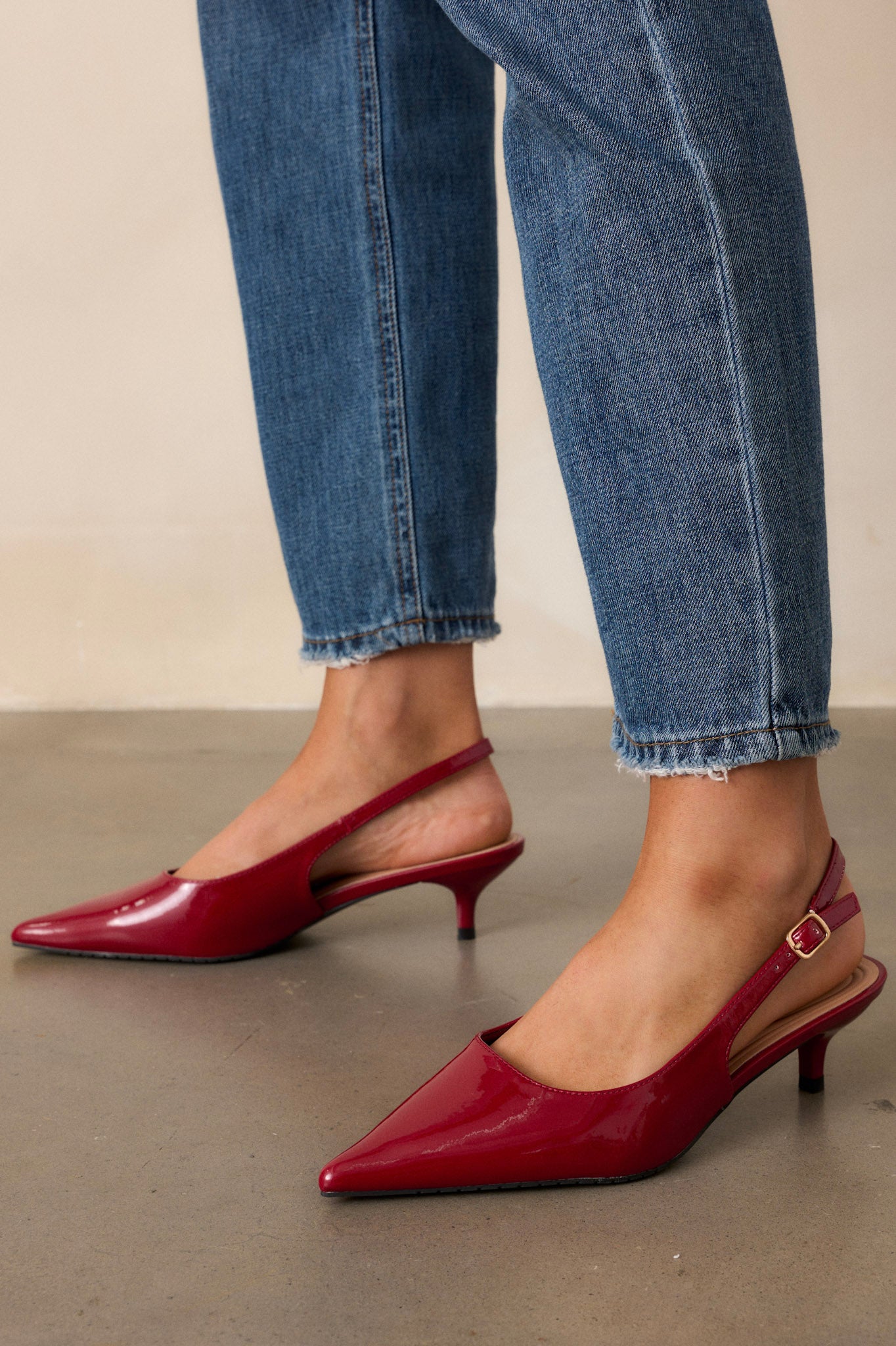 Full view of burgundy patent heels being worn, showing the pointed toe, adjustable slingback strap with a gold buckle, and the sleek kitten heel. 