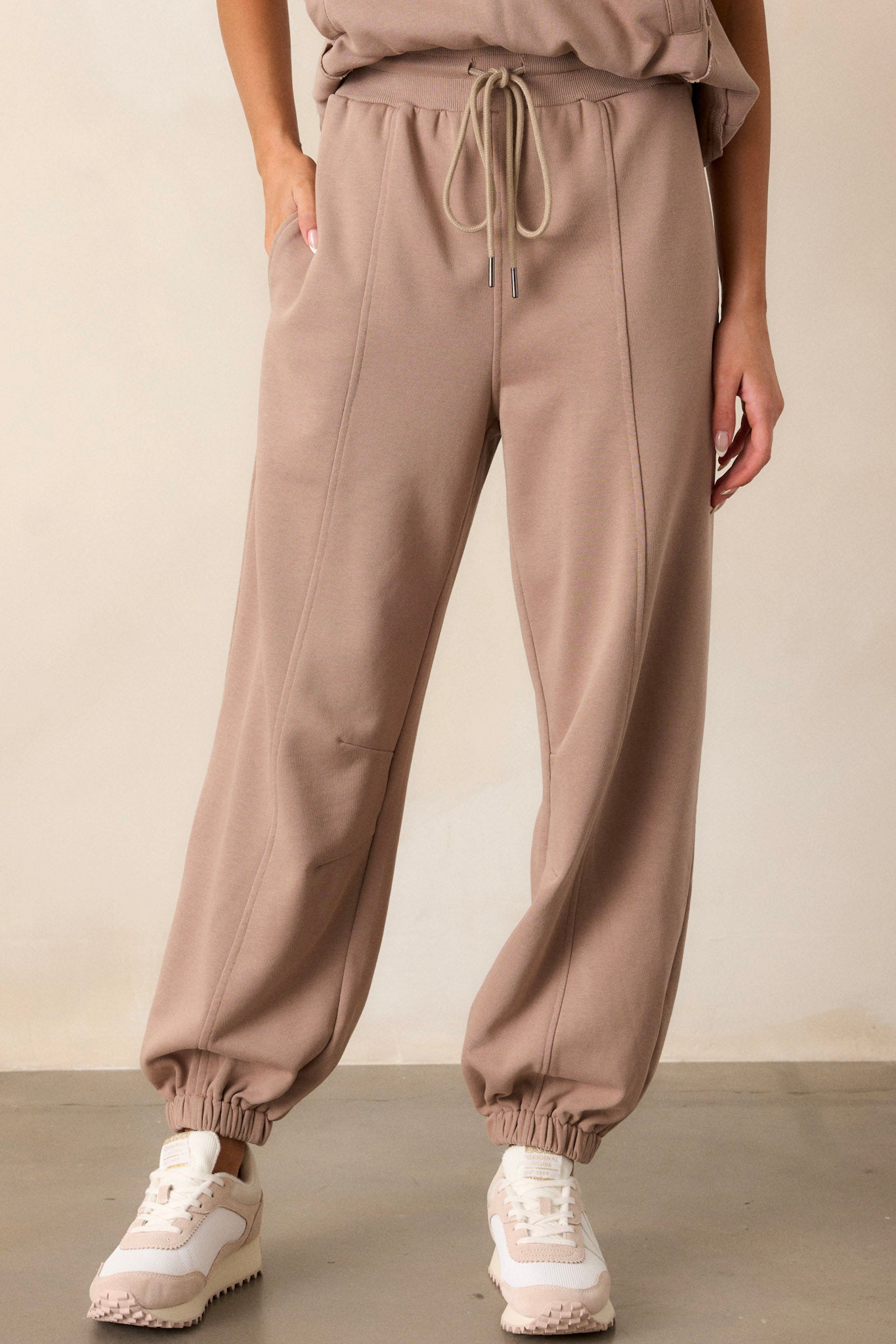 Front view of these light mocha joggers that feature a thick elastic waistband, an optional waist drawstring, functional hip pockets, a soft fabric, and elastic cuffed ankles.