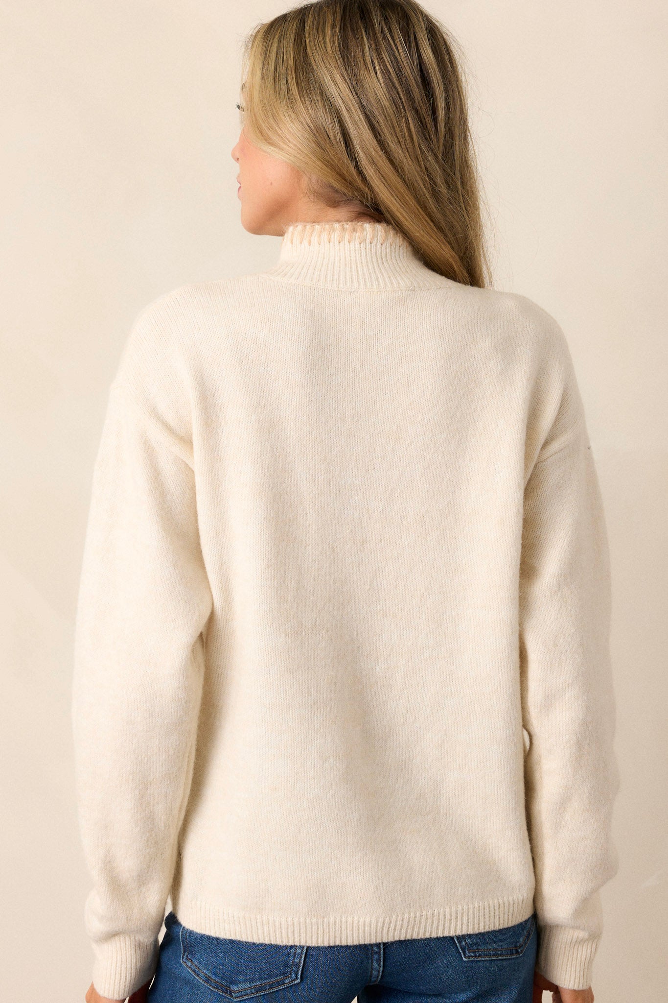 The back view of the ivory sweater, highlighting the ribbed bottom hem and the blanket stitch detailing running along the back seams.