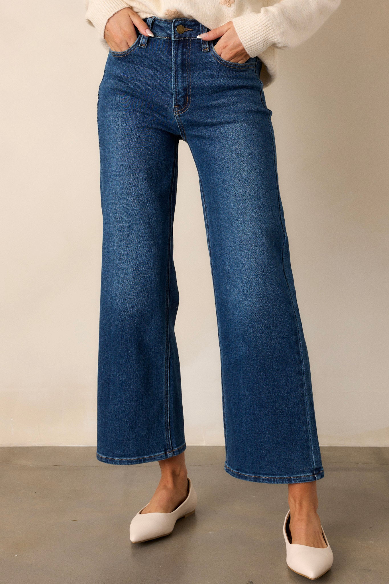 Cropped, dark wash blue jeans with functional front and back pockets, a zipper and button closure, a high rise fit, and a wide leg.