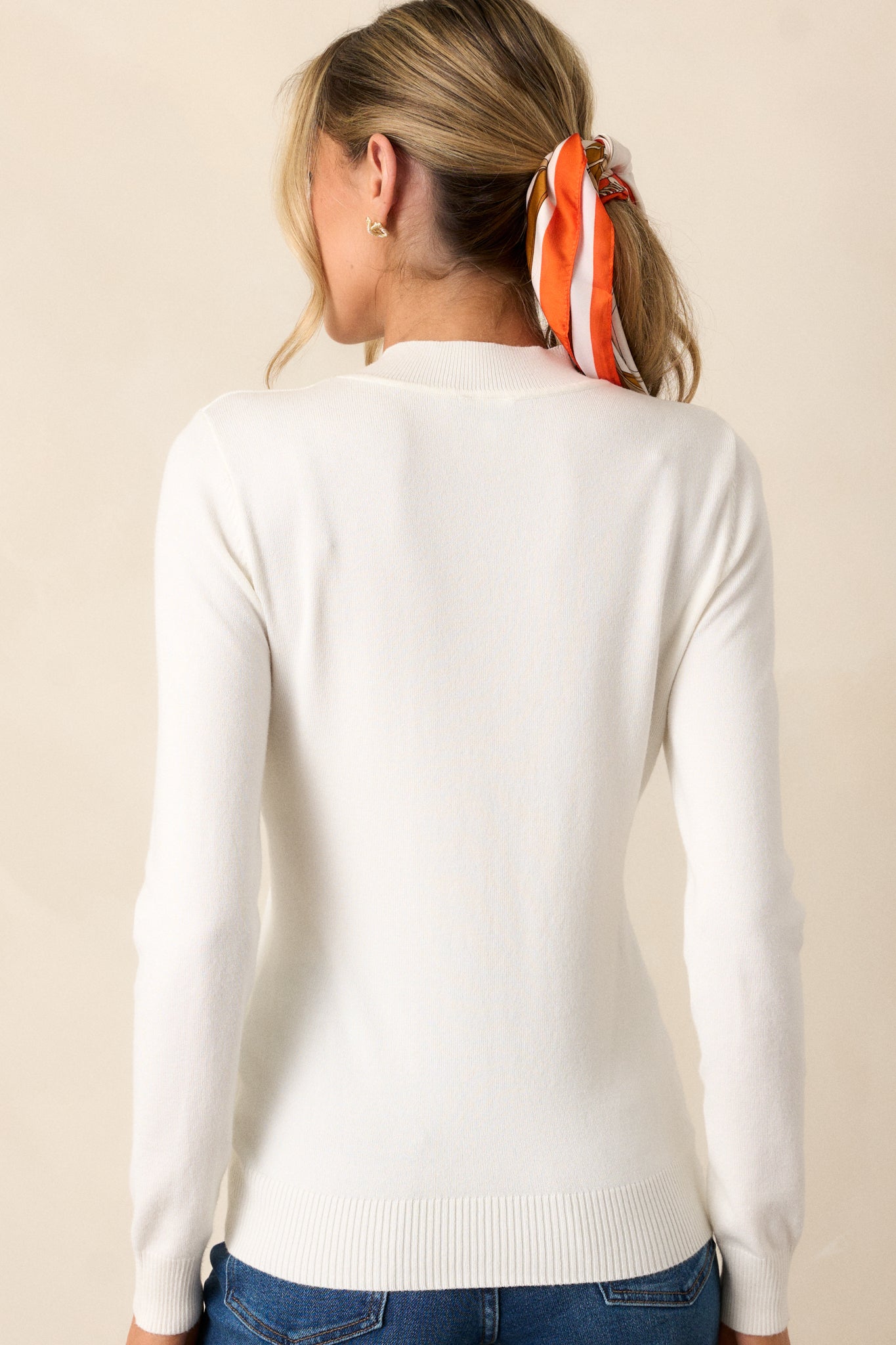 A view of the back of the ivory sweater top, showcasing the simple lines and the continuation of the ribbed hemline and sleeves.