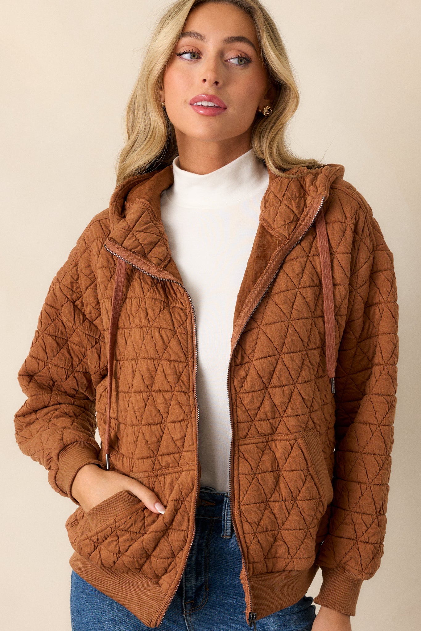 Full length view of the copper quilted jacket featuring a high neckline, zipper closure, functional hip pockets, a quilted design, a thick hem, and cuffed long sleeves