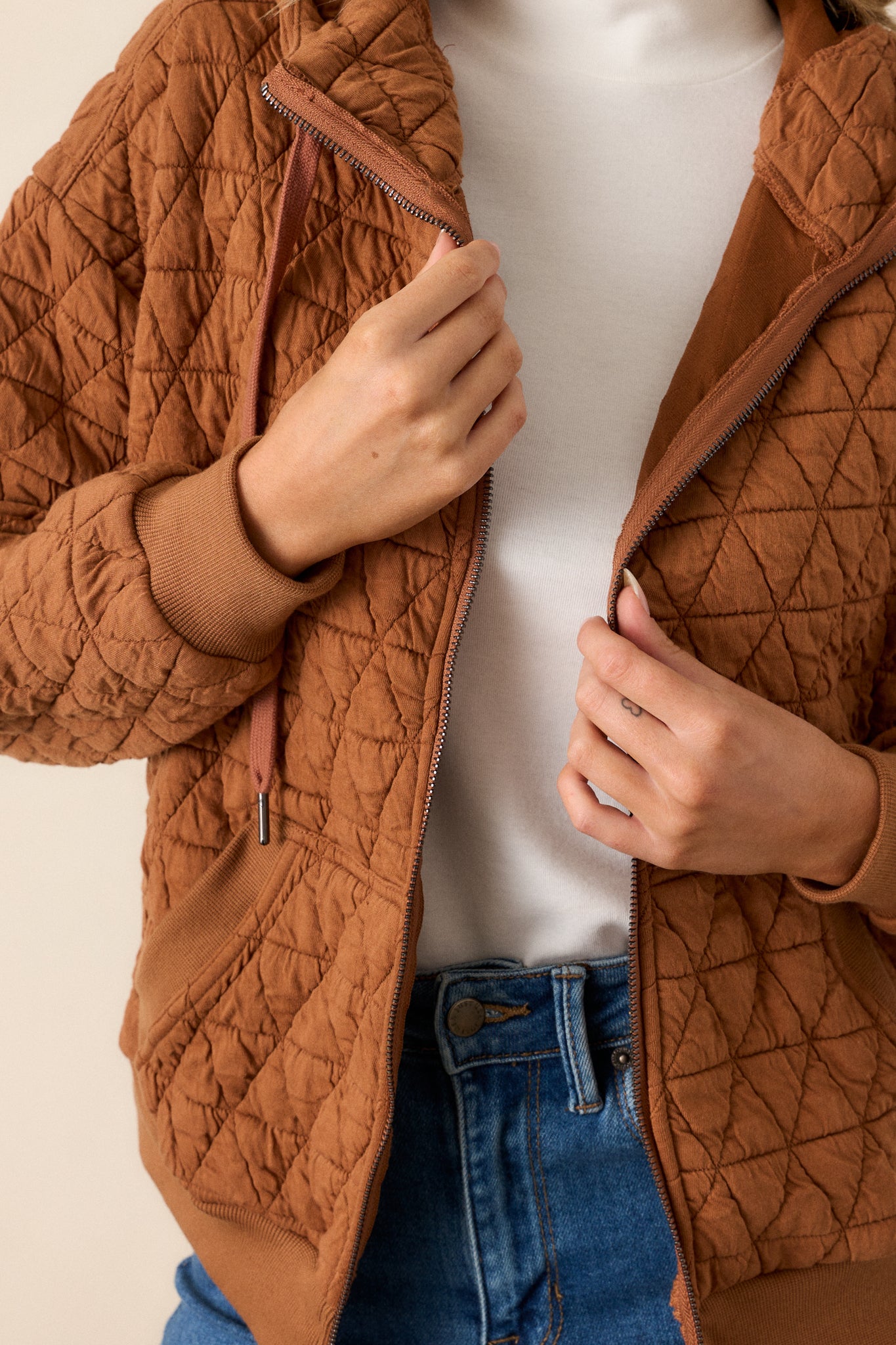 Close-up of the copper quilted jacket focusing on the high neckline, zipper closure, quilted texture, and the detailing on the thick hem and cuffed long sleeves.