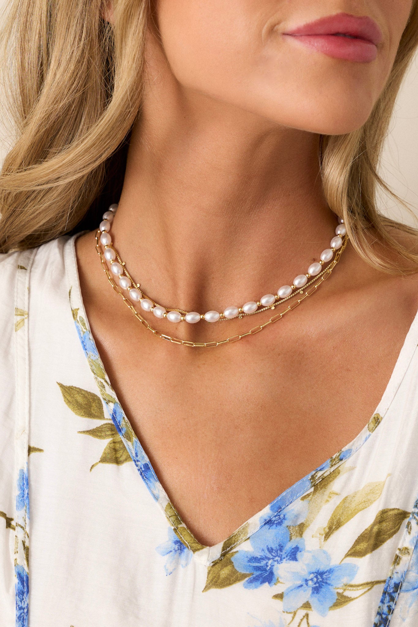 A close-up of the necklace’s layered design, highlighting the gold hardware, thin chains, and spherical ivory faux pearls.