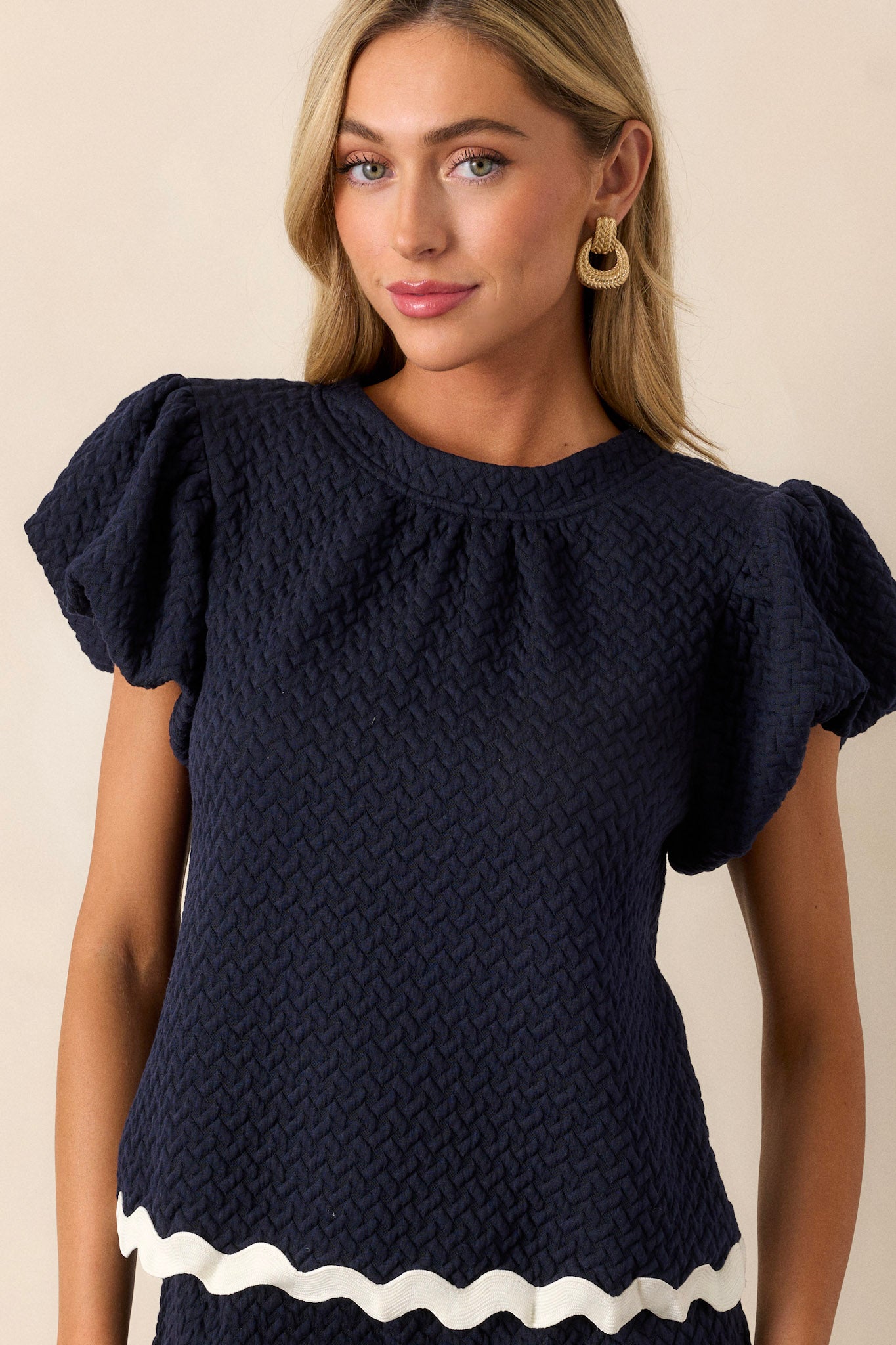 This navy top features a high rounded neckline, a quilted material, a contrasting scalloped hemline, and elastic cuffed puff sleeves.