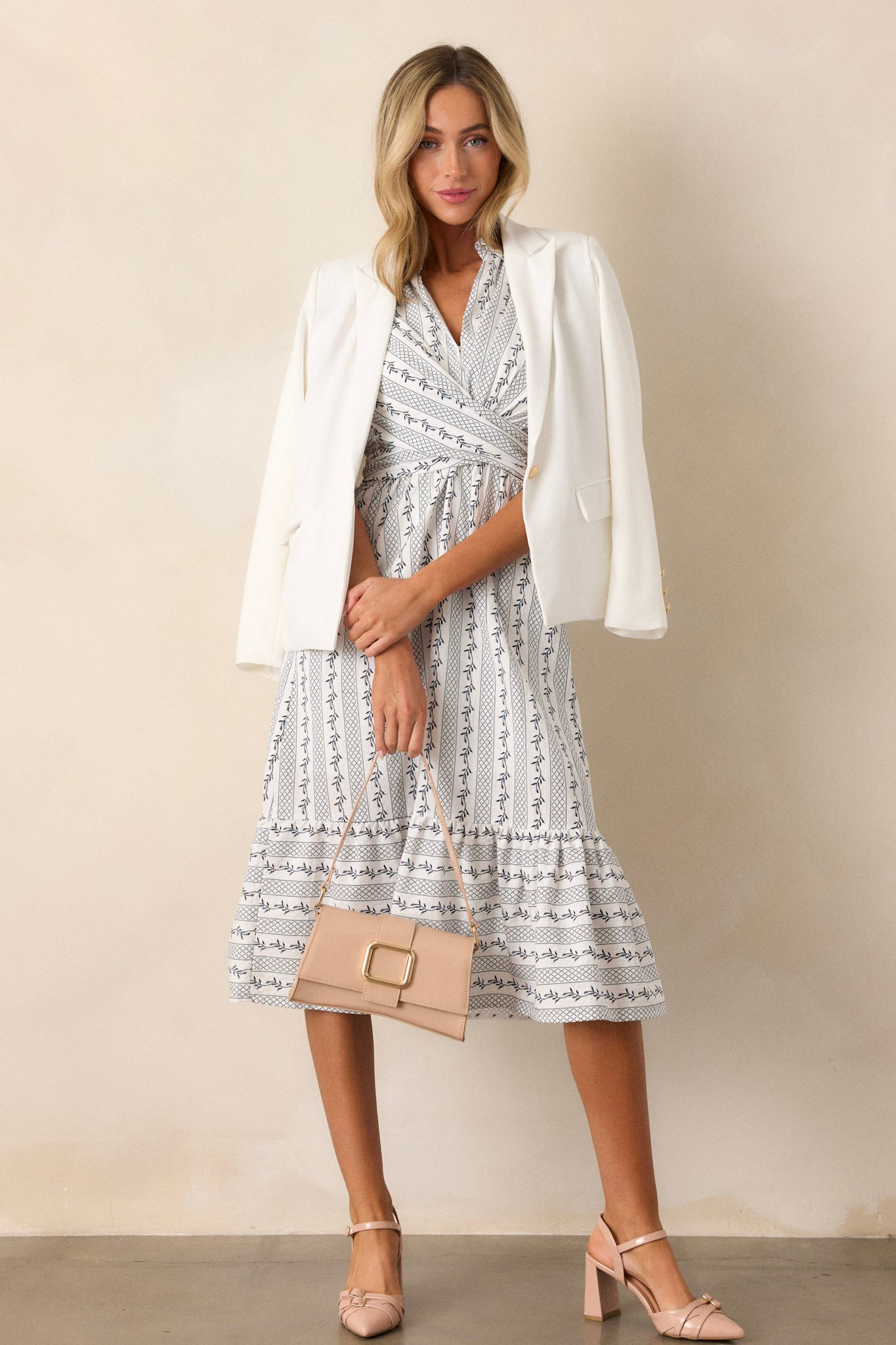 Action shot of an ivory dress displaying the flow and movement, highlighting the navy blue floral print, collared neckline, self-tie detail, and ruffled bottom edge.