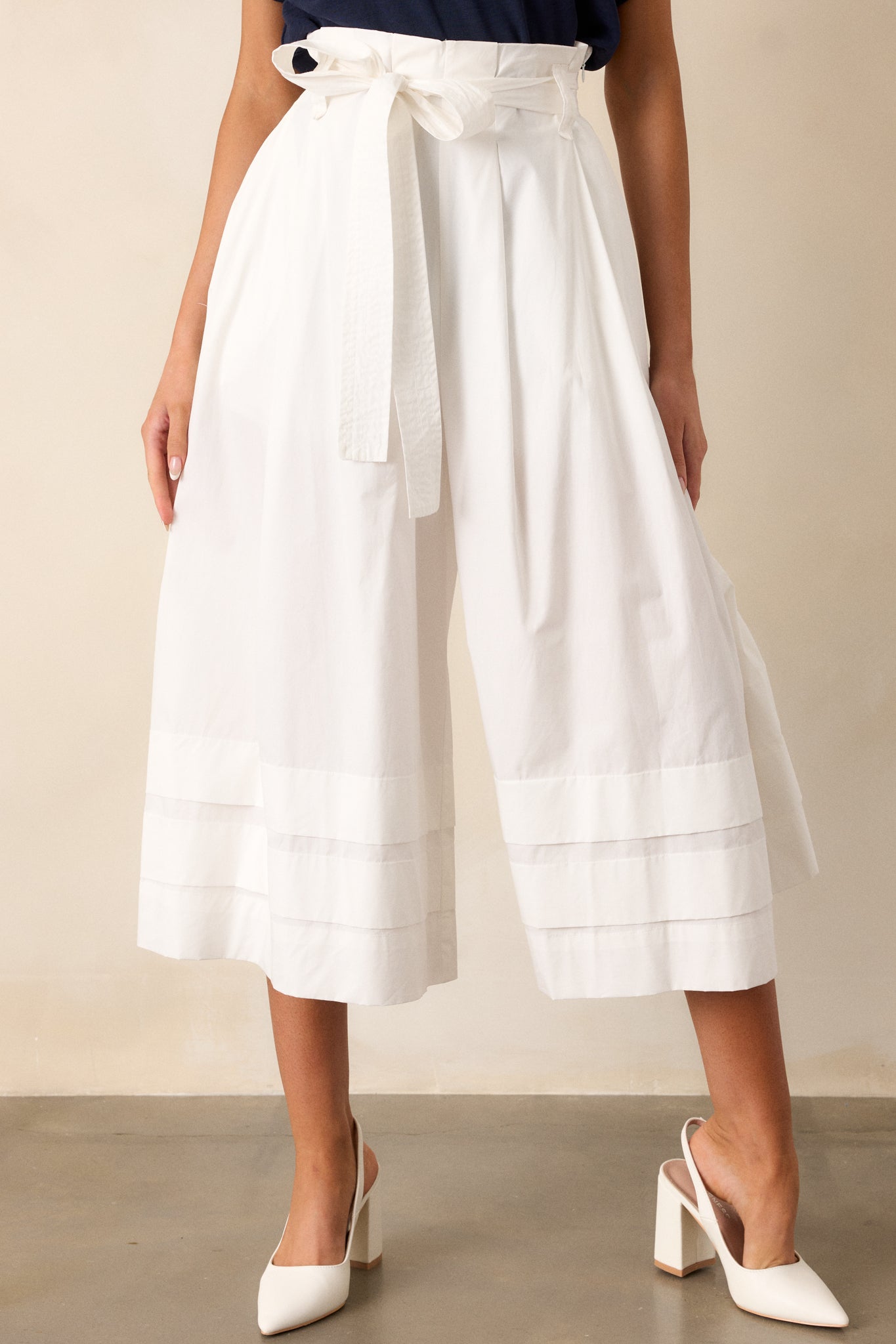 Front view of pants featuring a high waisted design, a discrete side zipper, belt loops, a self-tie belt, functional pockets, a thick and folded hemline, and an extremely wide leg.