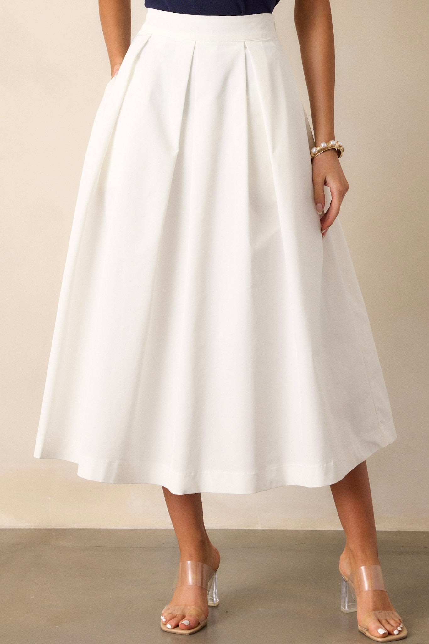 Front view of this white midi skirt that features a high waisted design, a discrete side zipper, and a thick waistline.