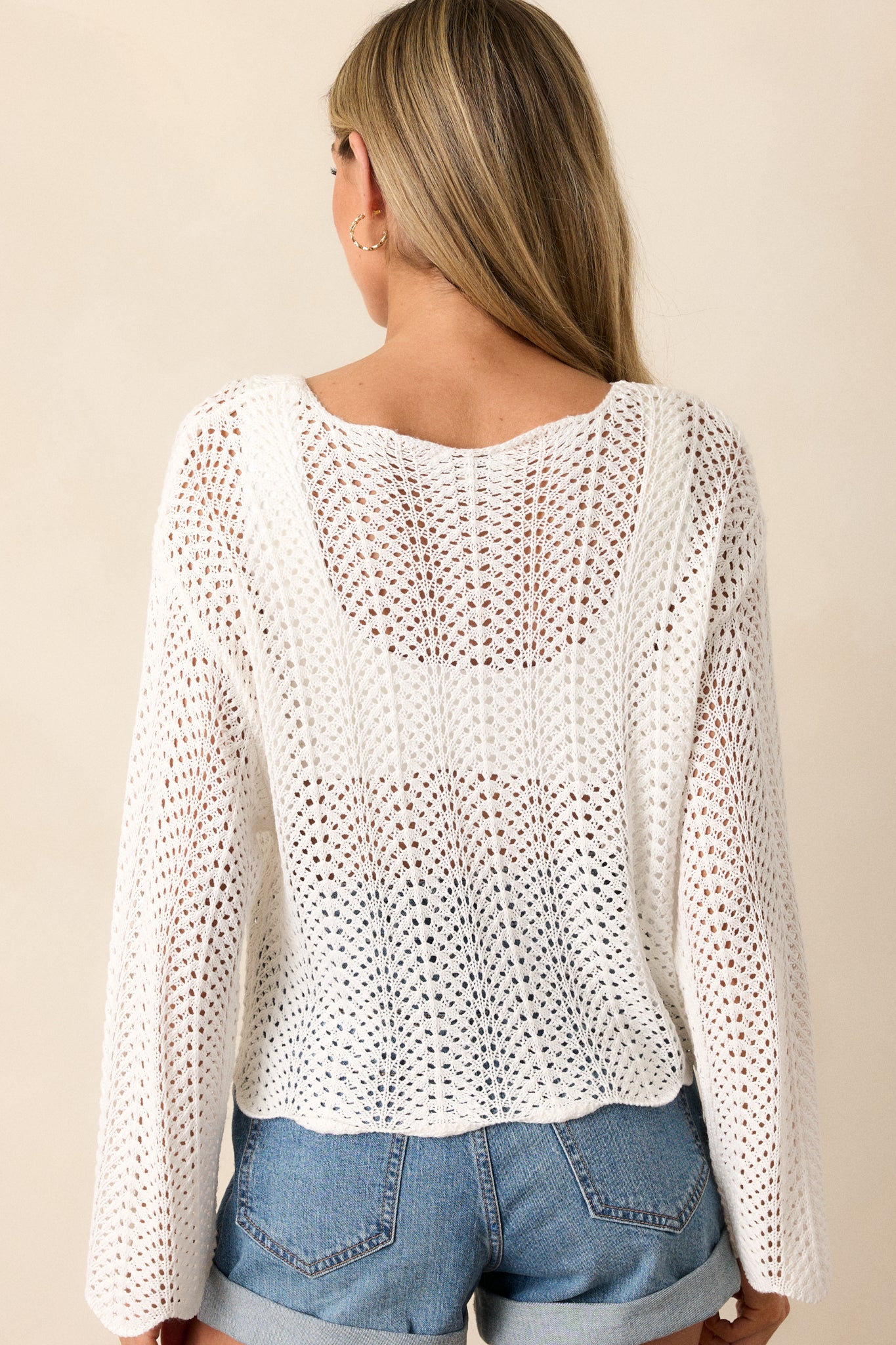 Back view of this top that features a high rounded neckline, a soft material, an open-knit crochet design, scalloped long sleeves, and a scalloped hemline.