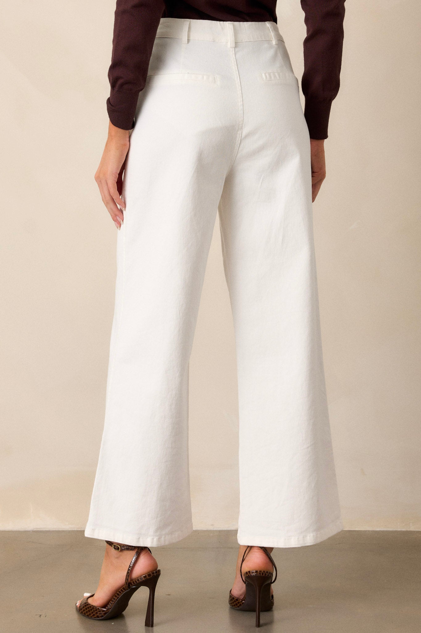 Back view of ivory jeans highlighting the high waisted design, belt loops, and faux back pockets.