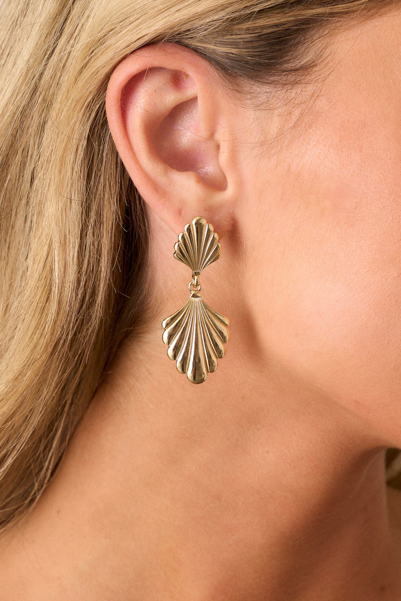 Close up view of these gold earrings feature a tiered drop design, textured shell-like shapes, and secure post backings.