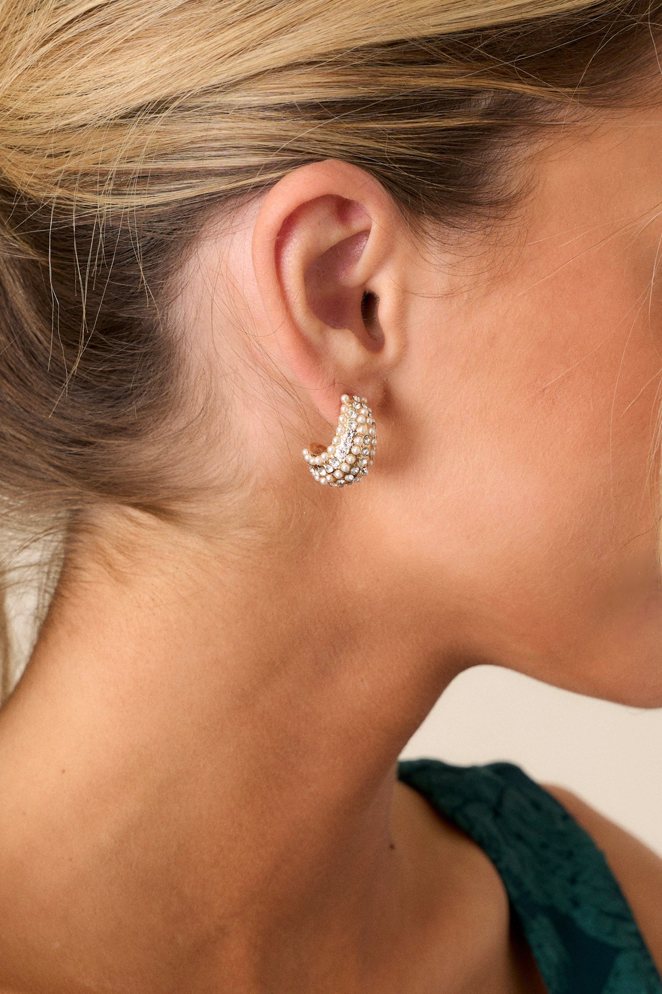 Gold earrings featuring an incomplete hoop design, adorned with horizontal lines of small faux ivory pearls and rhinestones, showcased against a neutral background.