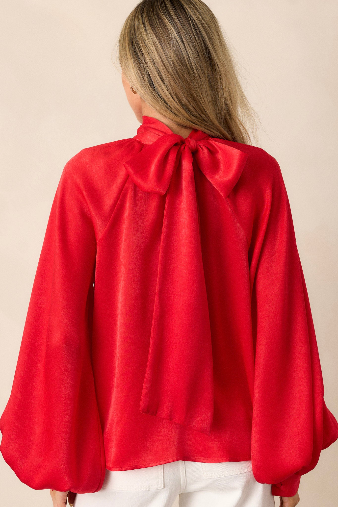 A view of the back of the top with the self-tie styled as a bow at the back, highlighting the flowy fit and smooth fabric from behind.