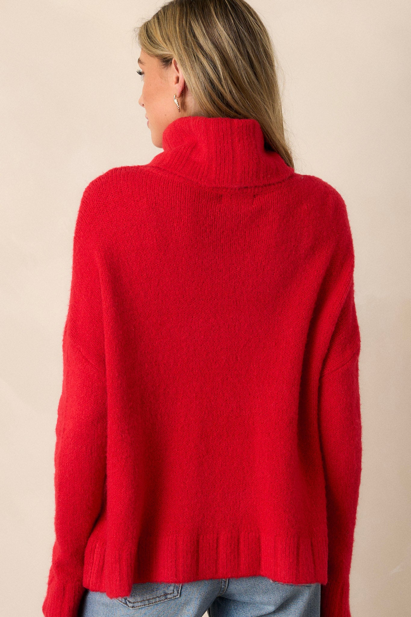 Back view of this sweater that features a very light eyelash knit design, a turtle cowl neckline, extremely dropped shoulders, and a slight high low hemline.