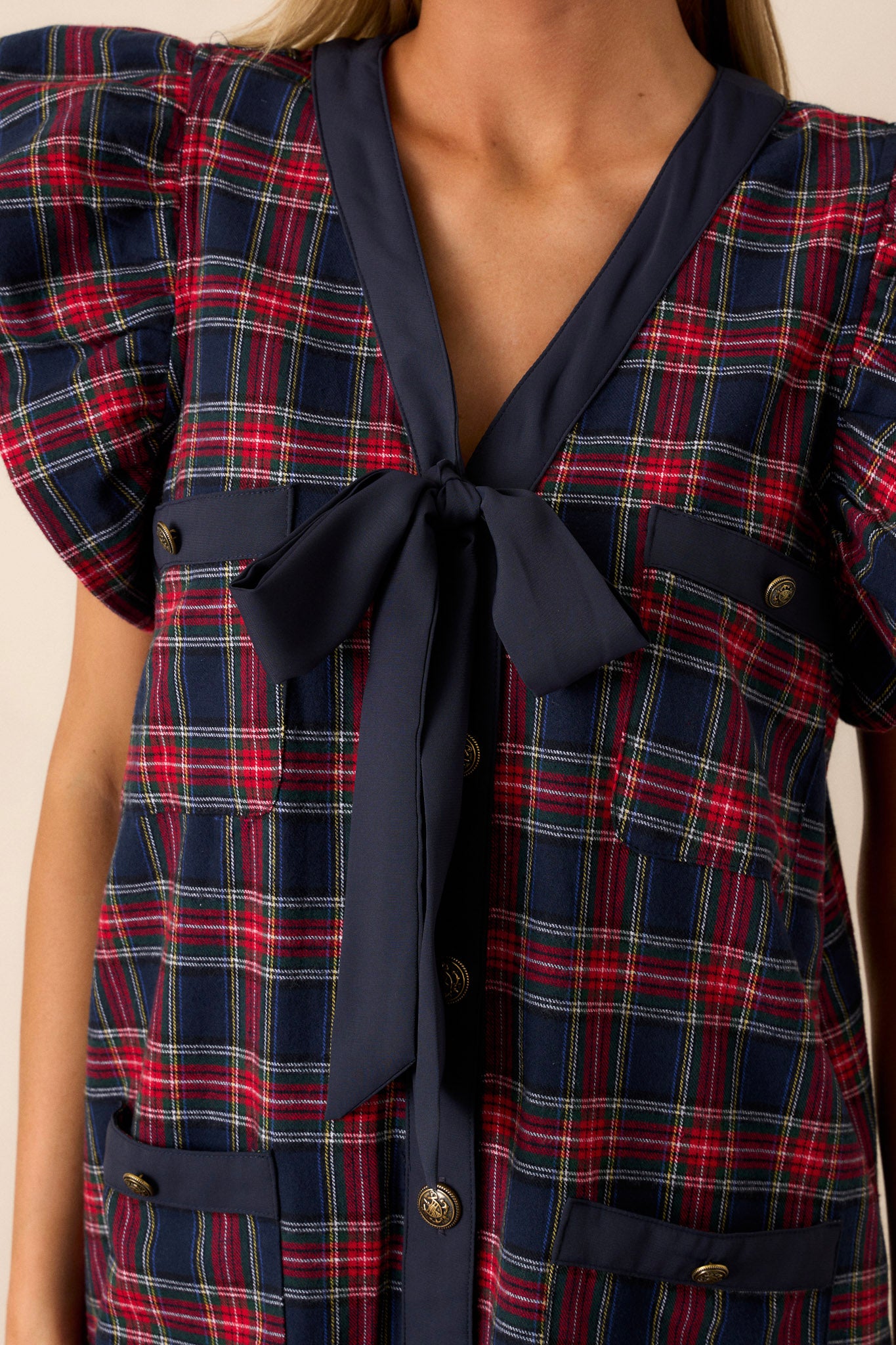 Detailed view of the navy bow v-neckline, antique gold buttons, and flutter sleeves on this navy plaid mini dress.