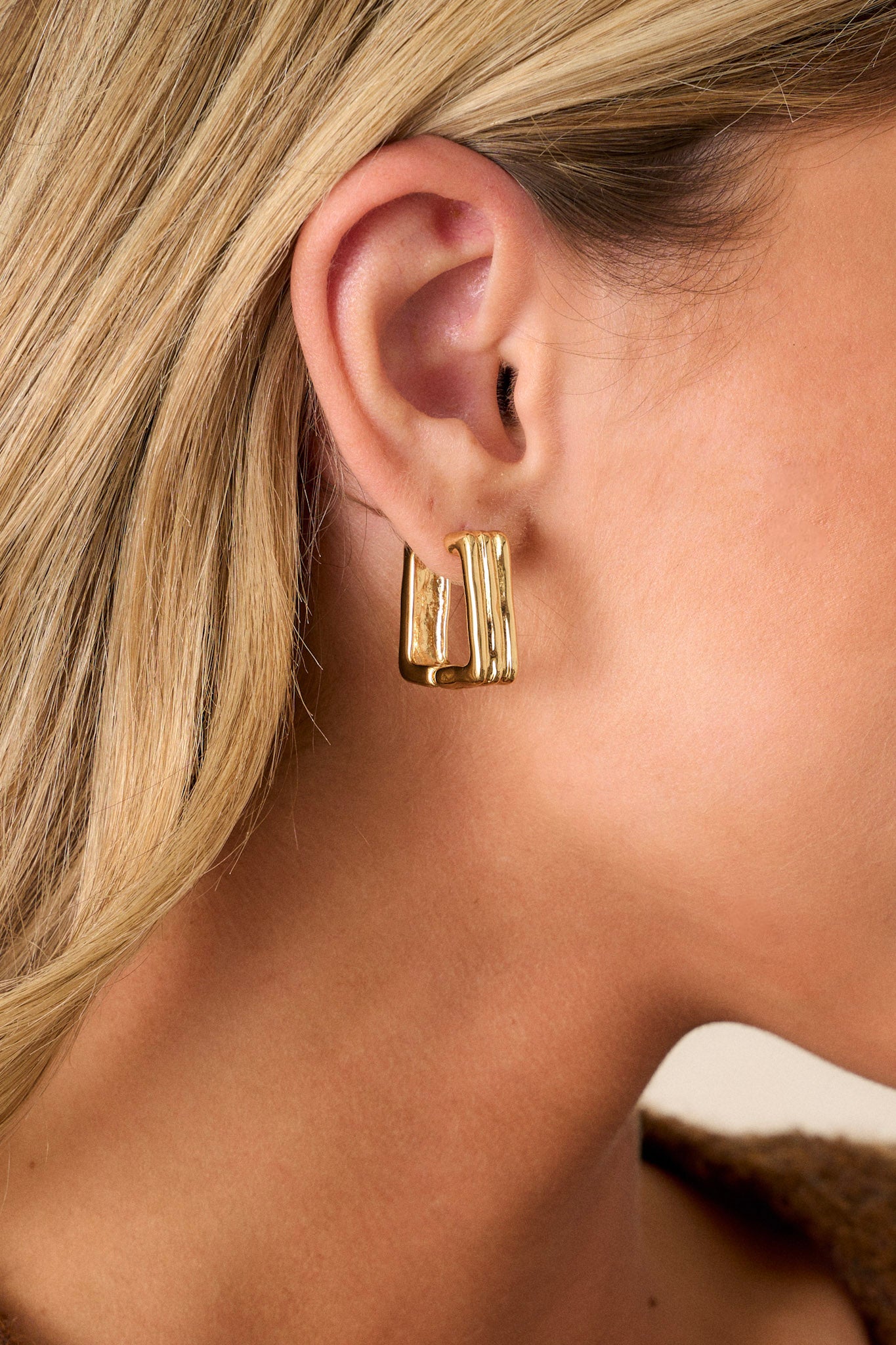 Close up of gold hoop earrings featuring gold hardware, a chunky design, a square shape, and hinged post.