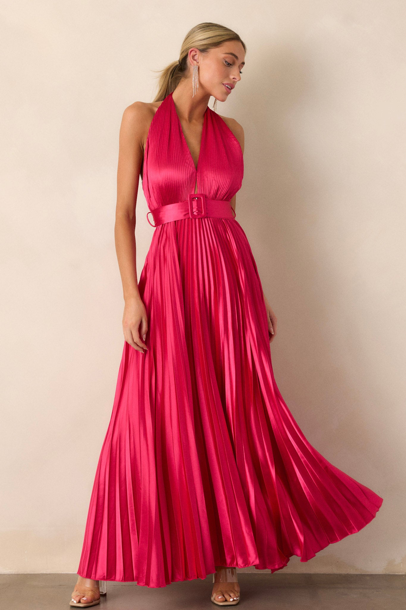 Full length view of a magenta pink dress featuring a vibrant pink color, beautiful pleats, a functional belt at the waist, a halter neck tie, and a functional zipper on the back