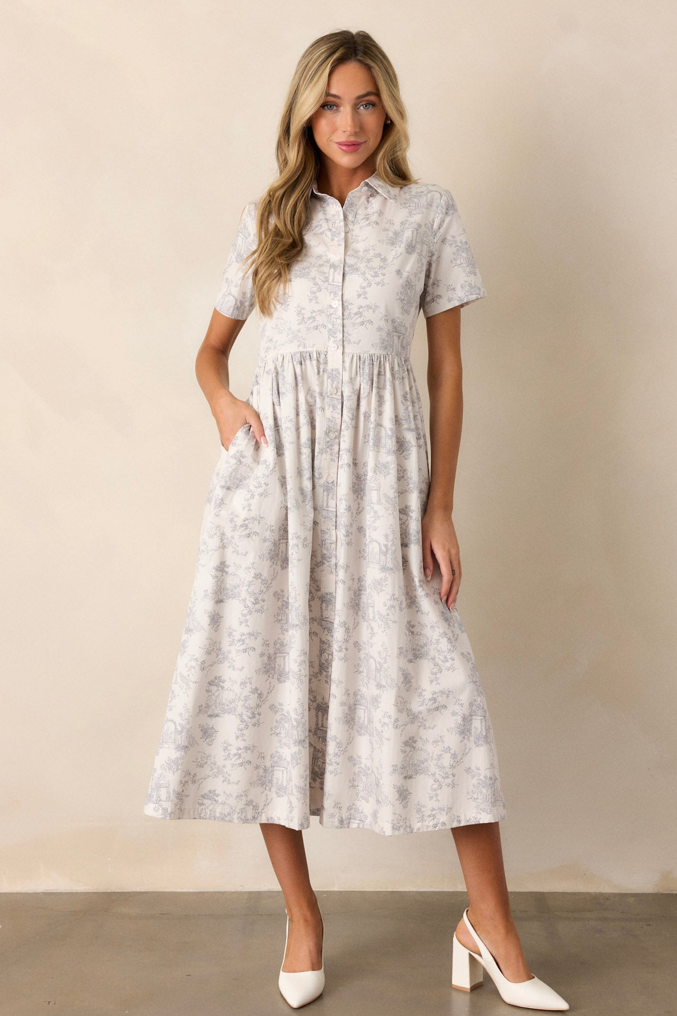 Full length view of a light grey maxi dress with a collared neckline, a functional button front, gathering at the waist, functional hip pockets, a gorgeous toile pattern, and a flowing silhouette