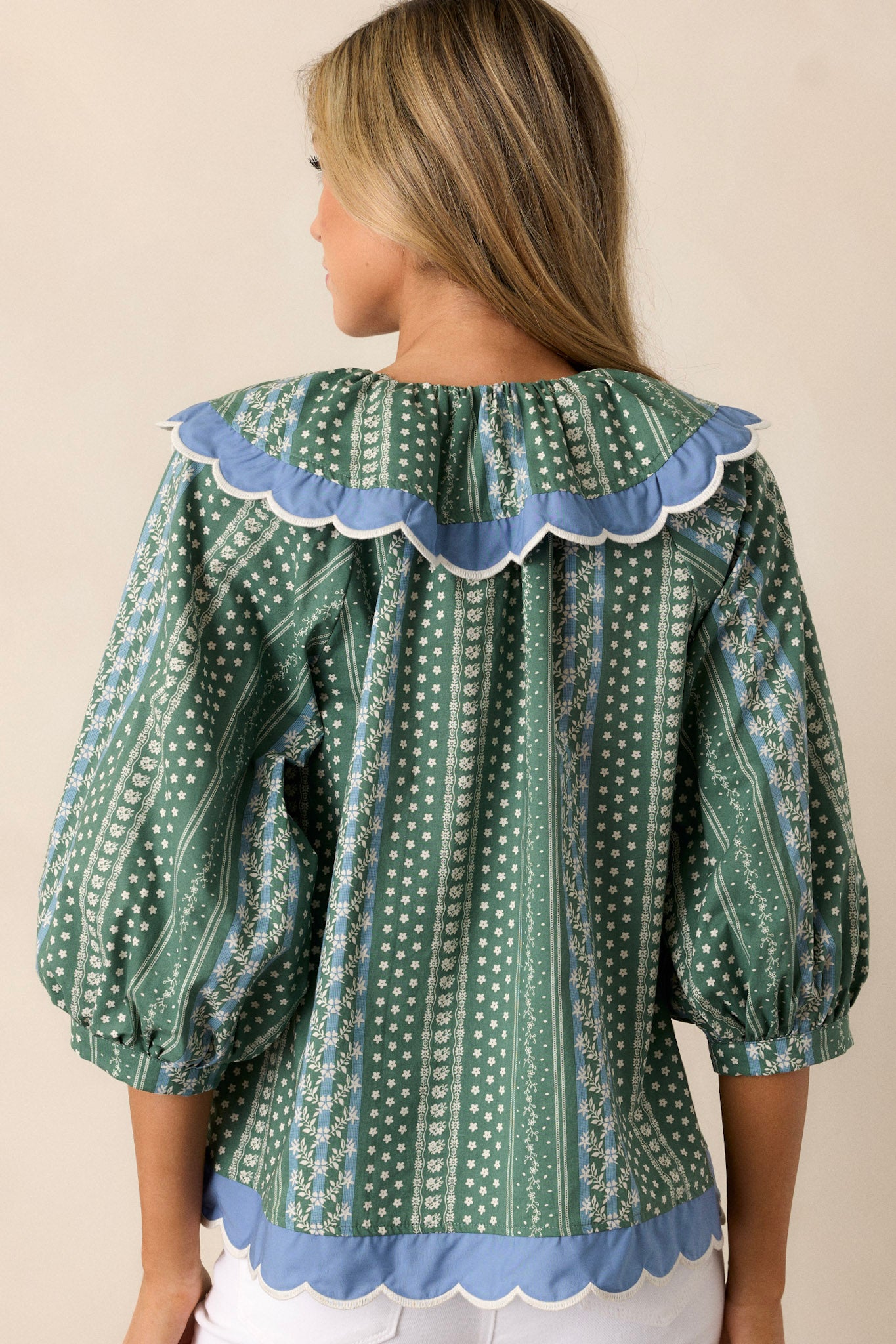 The back view of the green top, featuring the floral stripe print and the smooth scallop bottom hemline.