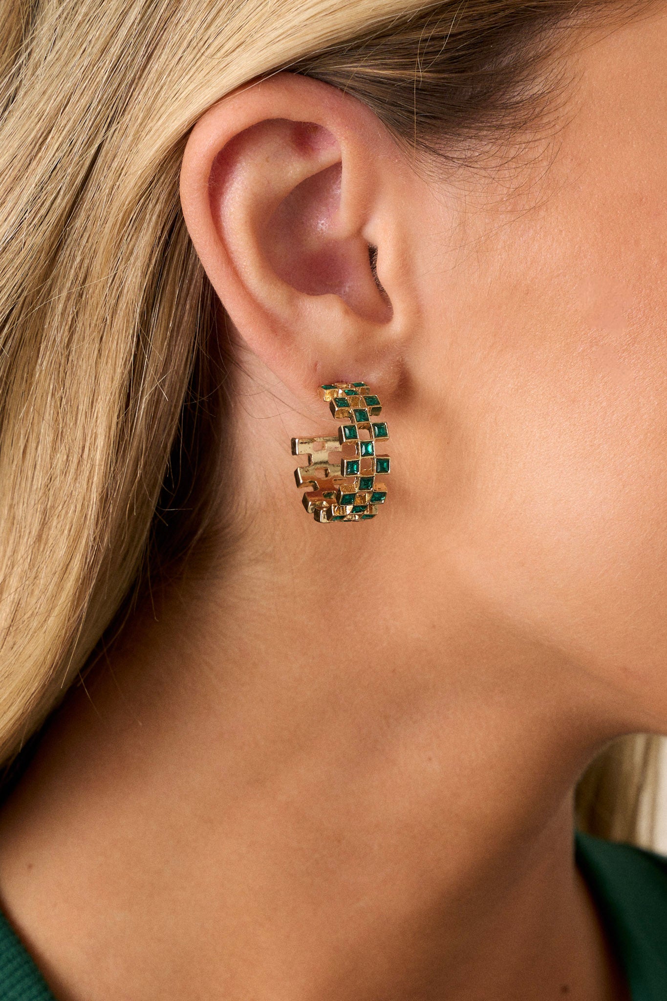 Close-up view of these earrings featuring an incomplete hoop design, checkered green rhinestones, gold hardware, and secure back postings.