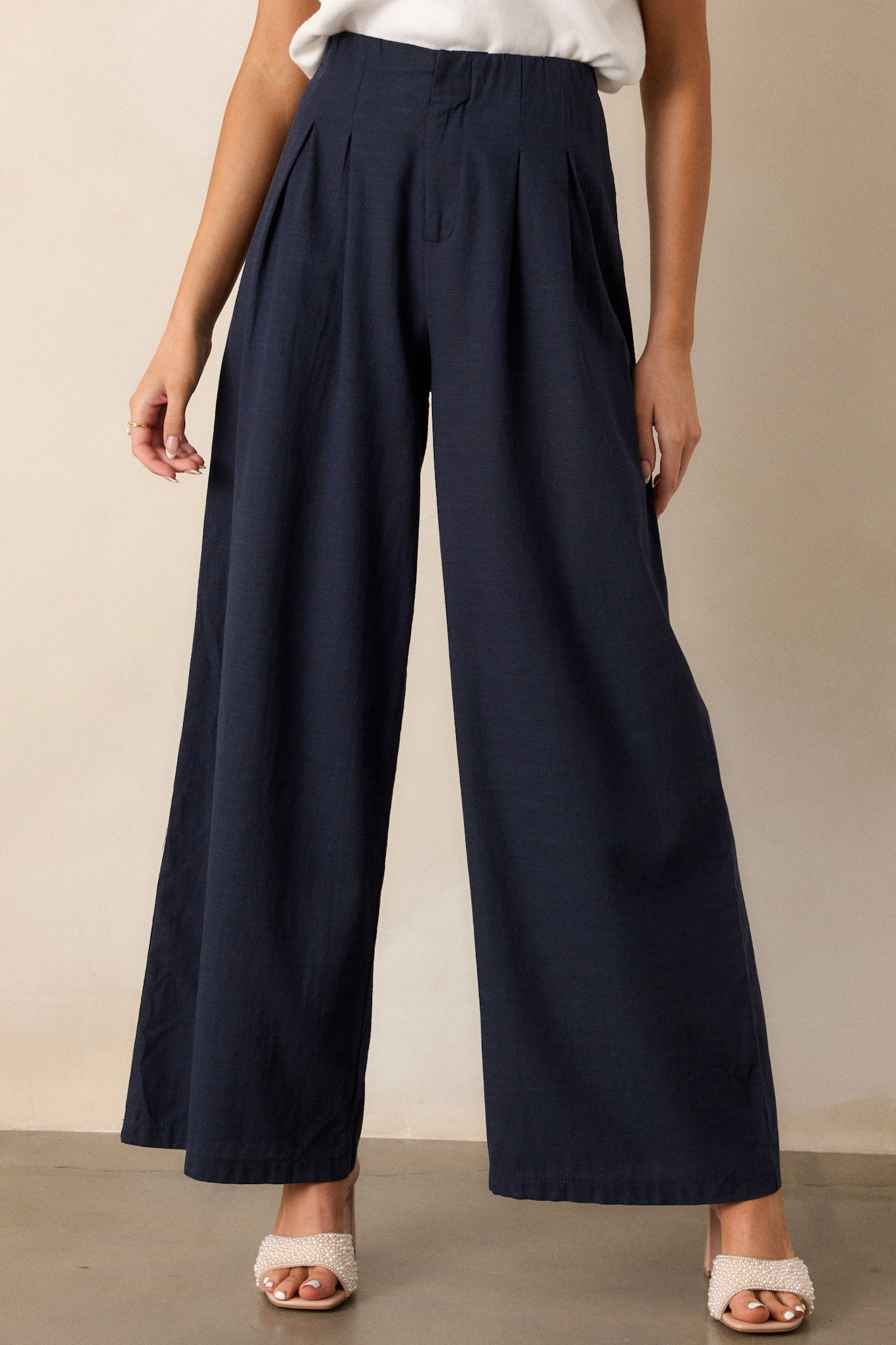 These navy straight leg pants feature a high waisted design, a button zipper closure, slight pleats, functional hip pockets and a straight leg.