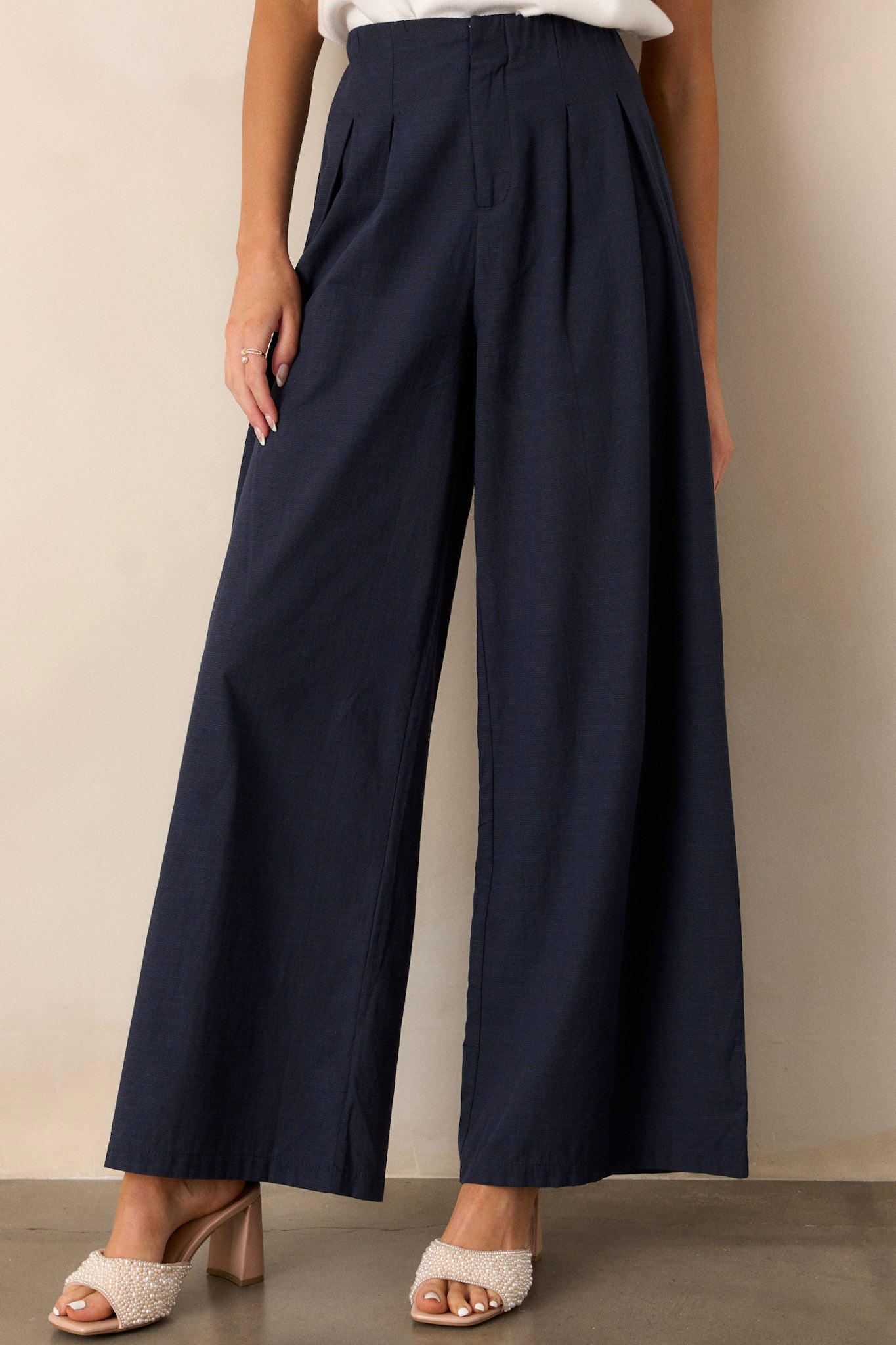 Front view of navy straight leg pants featuring a high waisted design, a button zipper closure, slight pleats, and functional hip pockets.