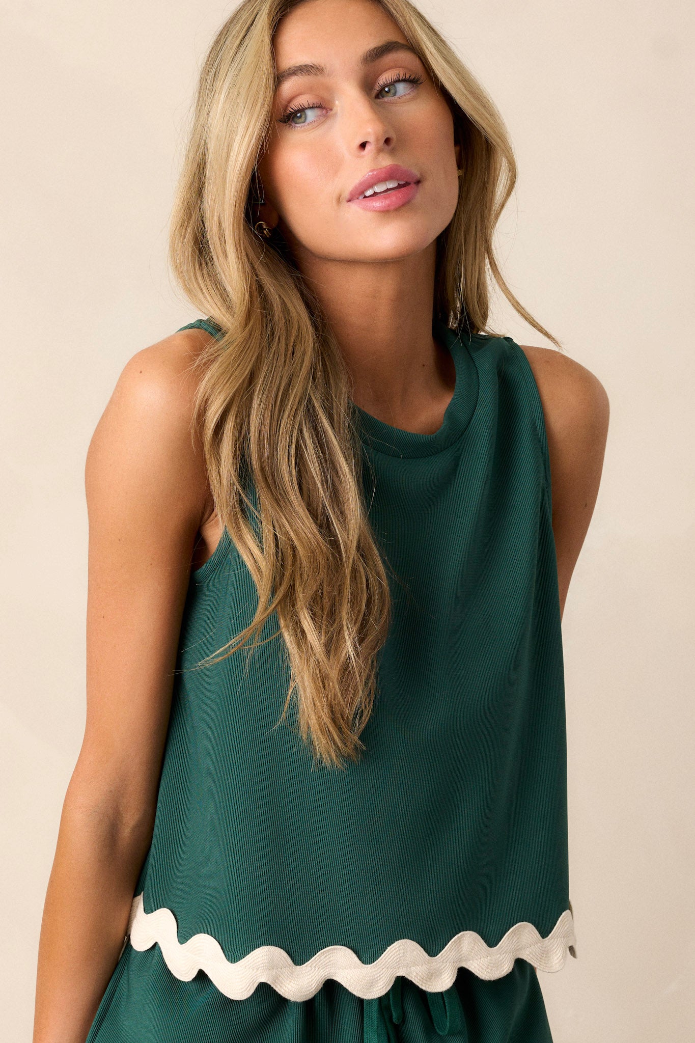 Front angled view of a hunter green tank top featuring a crew neckline, a ribbed texture, a ricrac hemline, and a sleeveless design