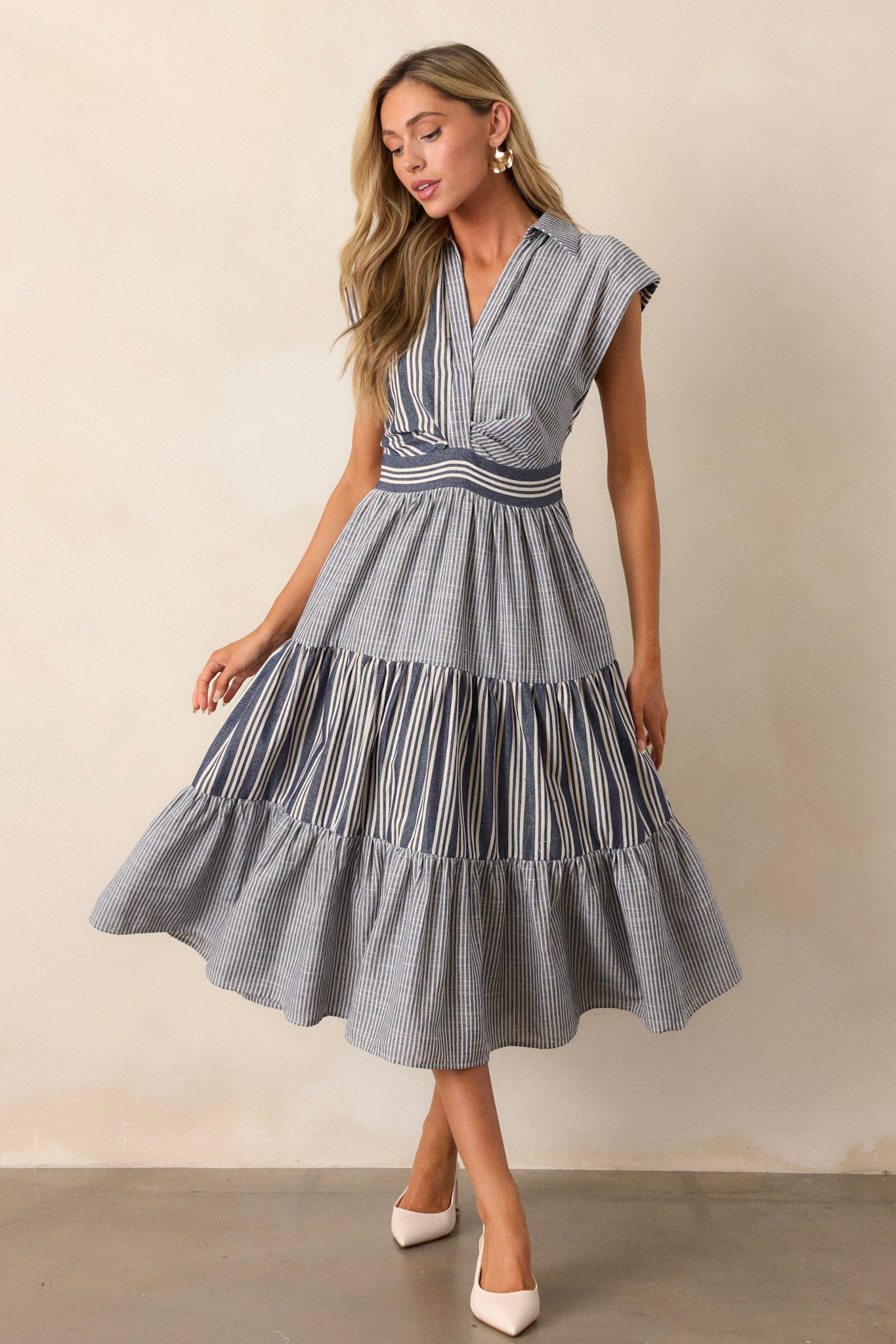 Navy dress showcasing a structured top with functional buttons, cap sleeves, and subtle shoulder padding, leading into a tiered skirt.