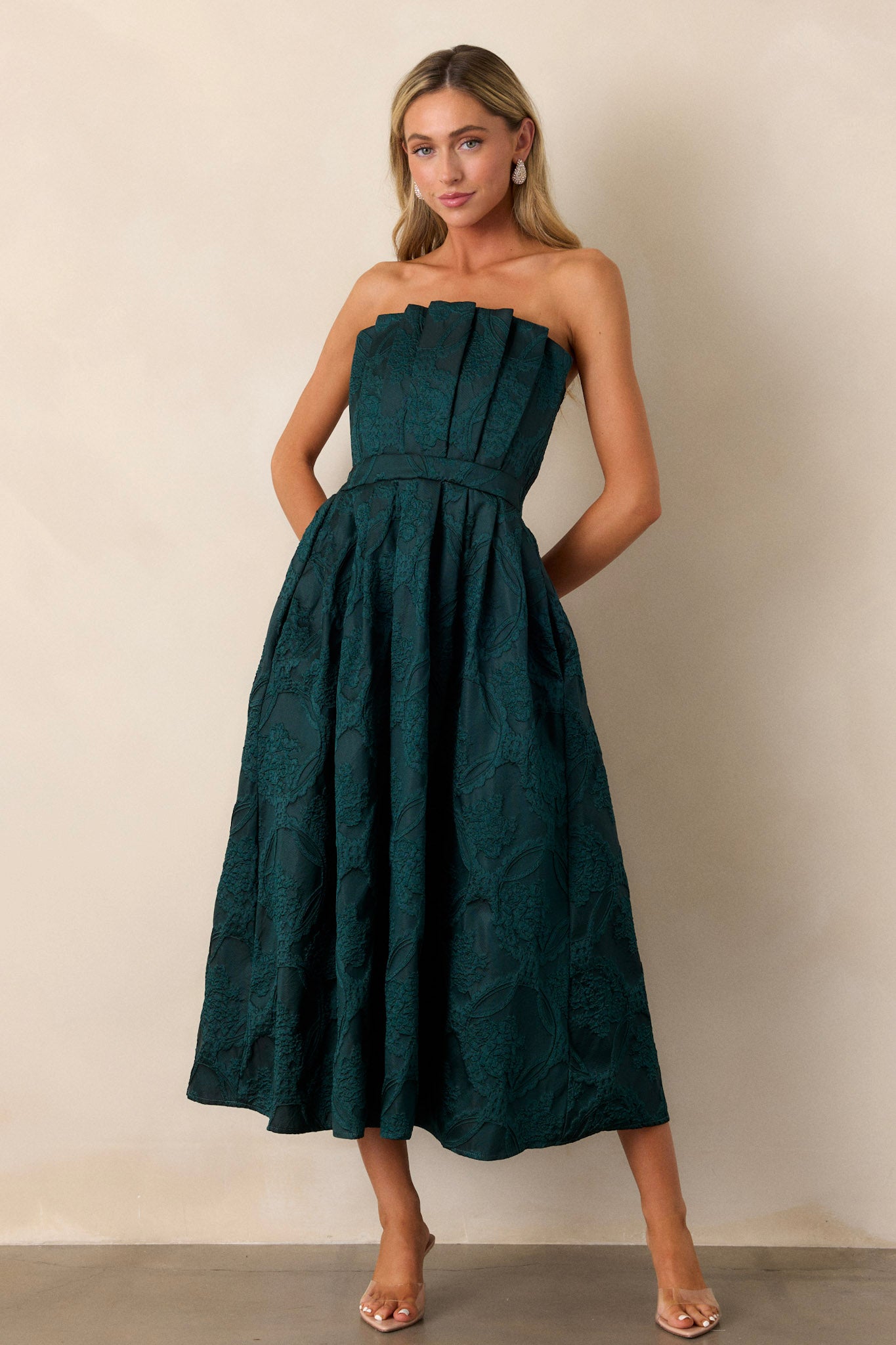 Full-body shot of the green dress, showcasing the pleated bodice, functional pockets at the hips, and the sleek strapless design.