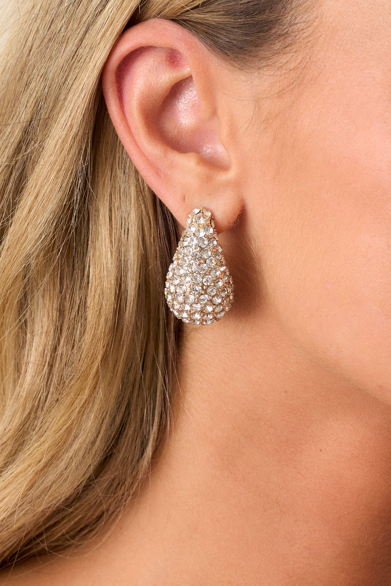 A front view of the gold earrings showcasing the bold teardrop design and the shimmering clear rhinestones that catch the light beautifully.