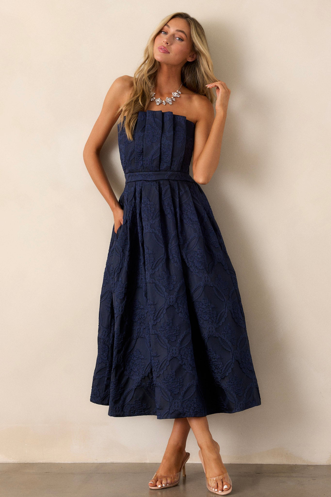 This navy midi dress features a pleated bodice, a slightly pleated skirt, a jacquard design, functional hip pockets, a smocked back, a discrete back zipper and a strapless design.