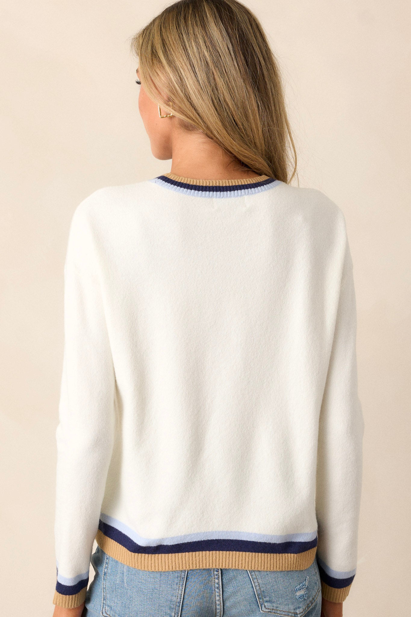 Back view of ivory sweater, showcasing the cozy knit fabric and striped navy and yellow ribbed hem at the bottom.