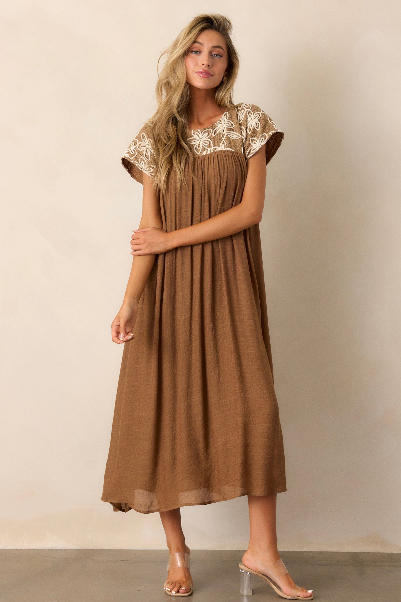 Tan midi dress with a high rounded neckline, detailed with an embroidered floral pattern and a flowing silhouette.