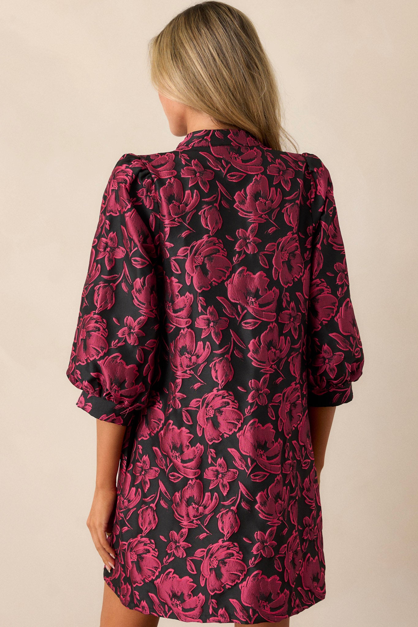 A view of the back of the dress, highlighting the balloon sleeves and how the floral jacquard fabric continues across the back, ending at the mini-length hem.