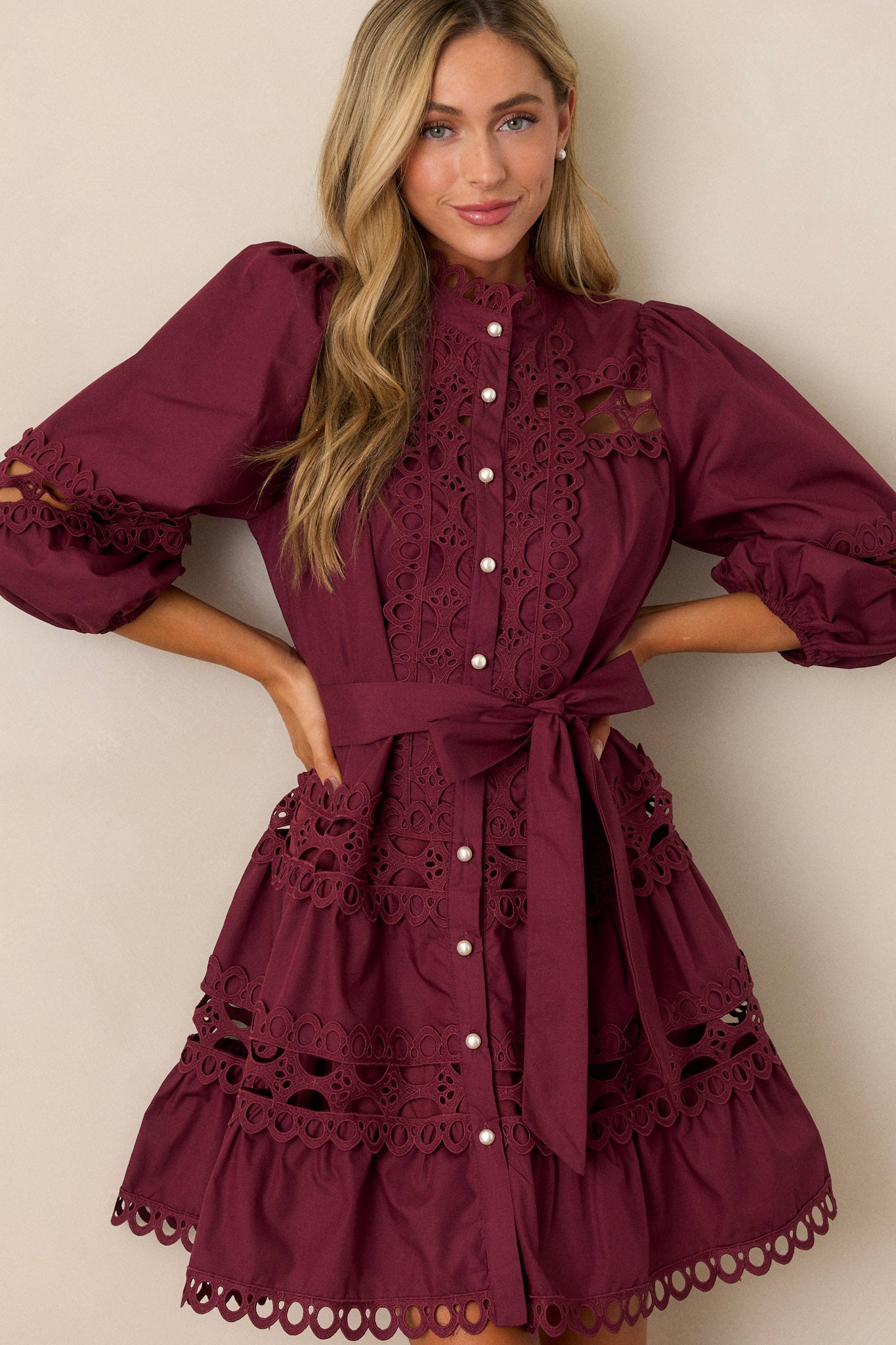 Font view of this  plum mini dress featuring a high neckline, a functional button front with faux pearl buttons, an optional self-tie belt, elastic cuffed 3/4 length sleeves, and eyelet detailing throughout.