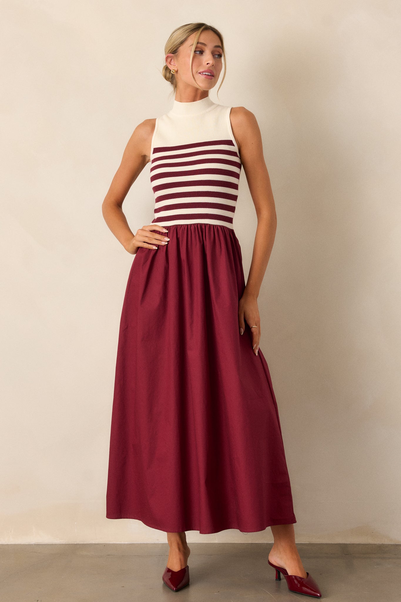 Full body view of this burgundy stripe maxi dress that features a high neckline, a striped sweater bodice, and a flowy skirt.