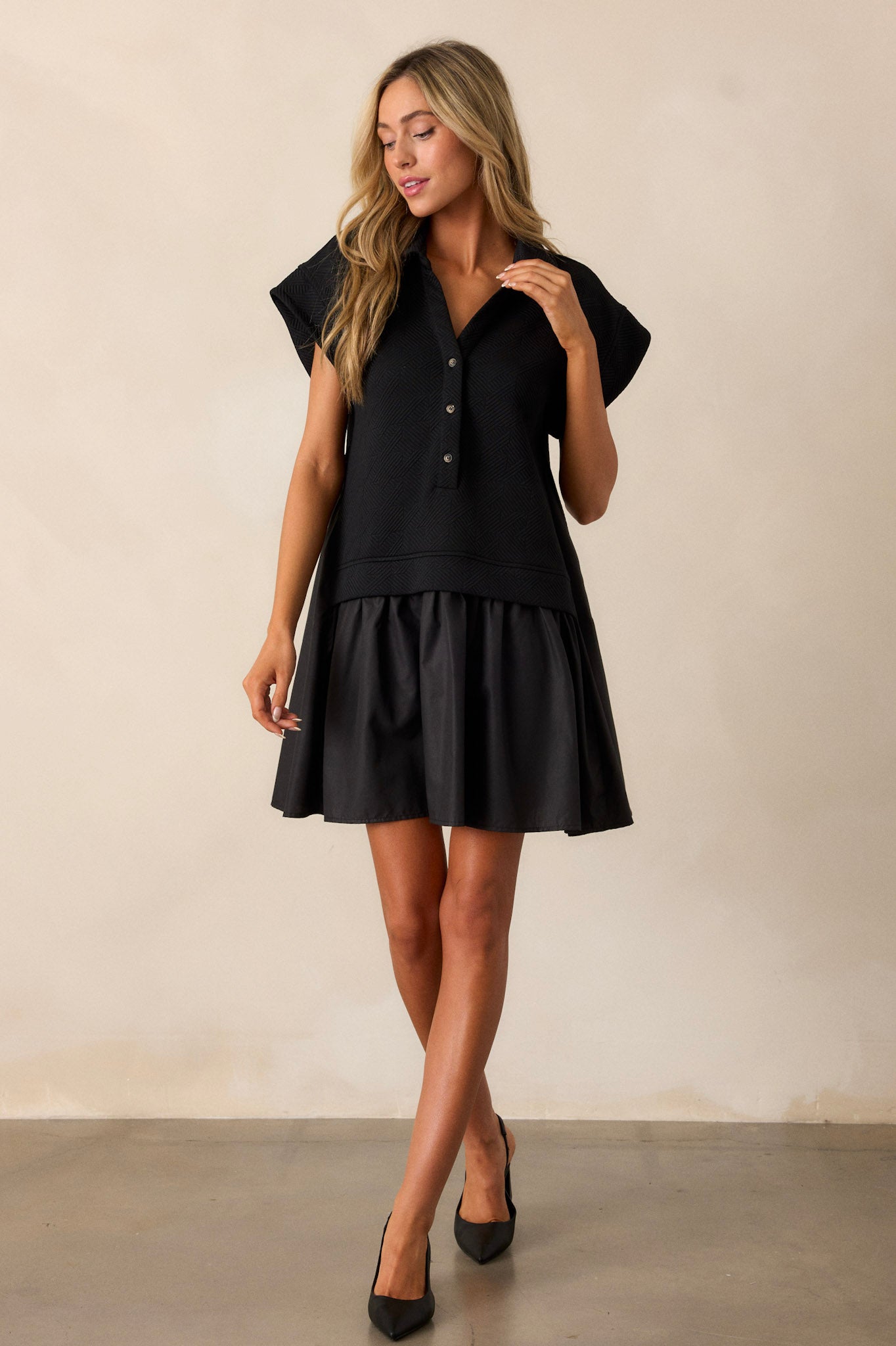 Full body view of a black quilted dress displaying the fit and movement, highlighting the collared v-neckline, functional button front, quilted bodice, tiered design, and short sleeves.