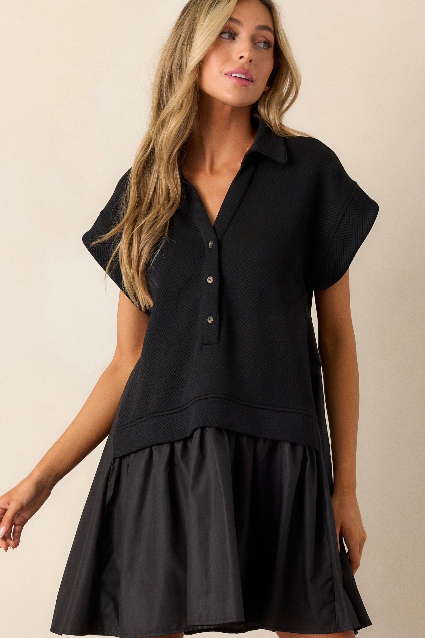 Front view of a black quilted dress featuring a collared v-neckline, a functional button front, a quilted bodice, a tiered design, and short sleeves.