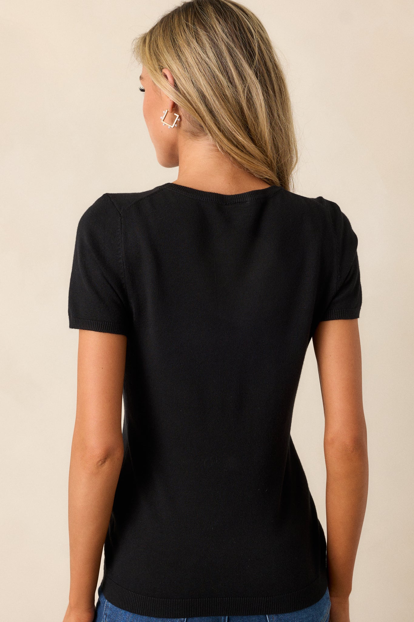 Rear view of the black sweater top, highlighting its simple back design, soft fabric, and ribbed hem.